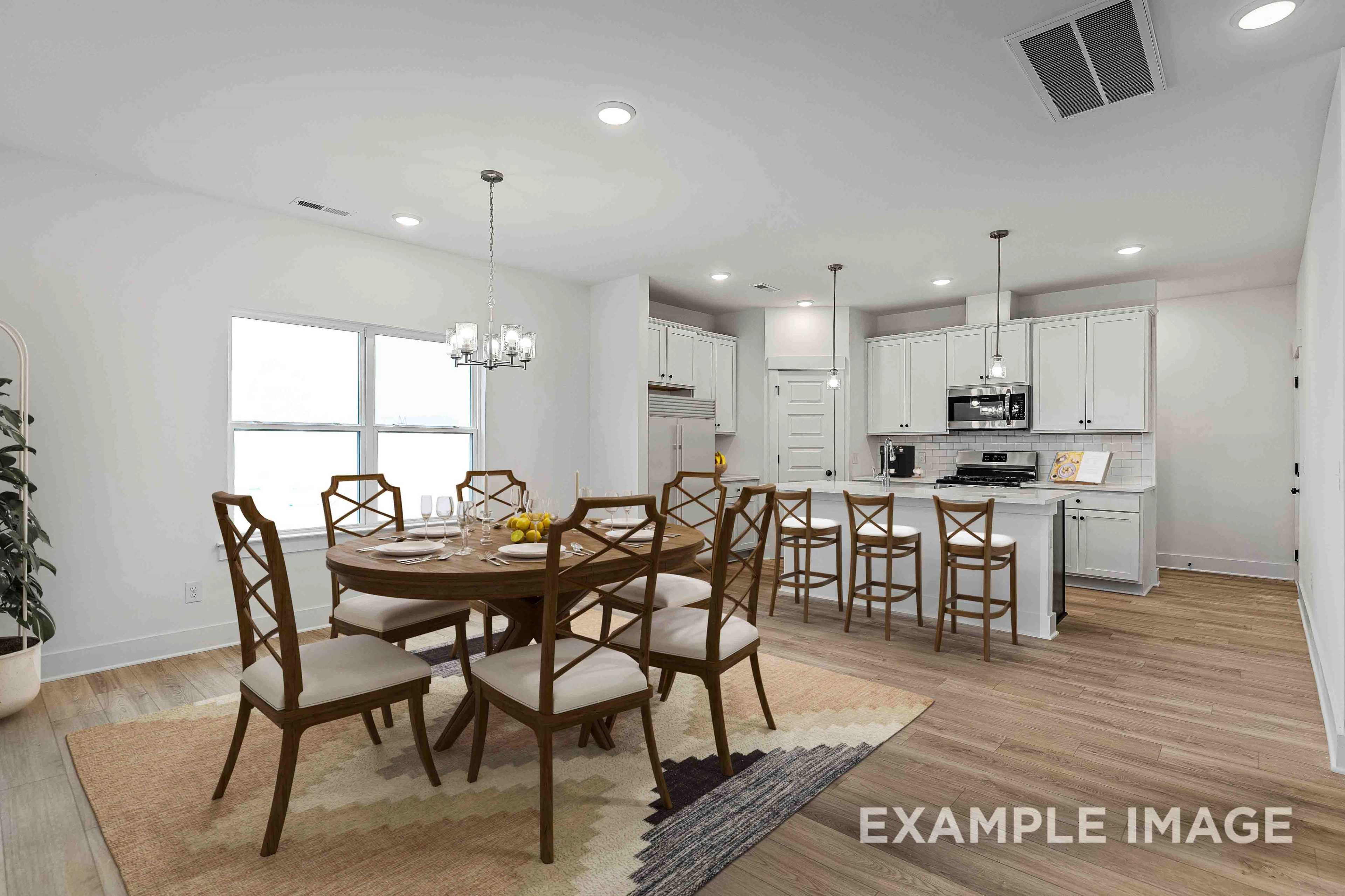 Open-concept dining room in The Charleston home design with round wooden table, chandelier, and adjacent white kitchen island