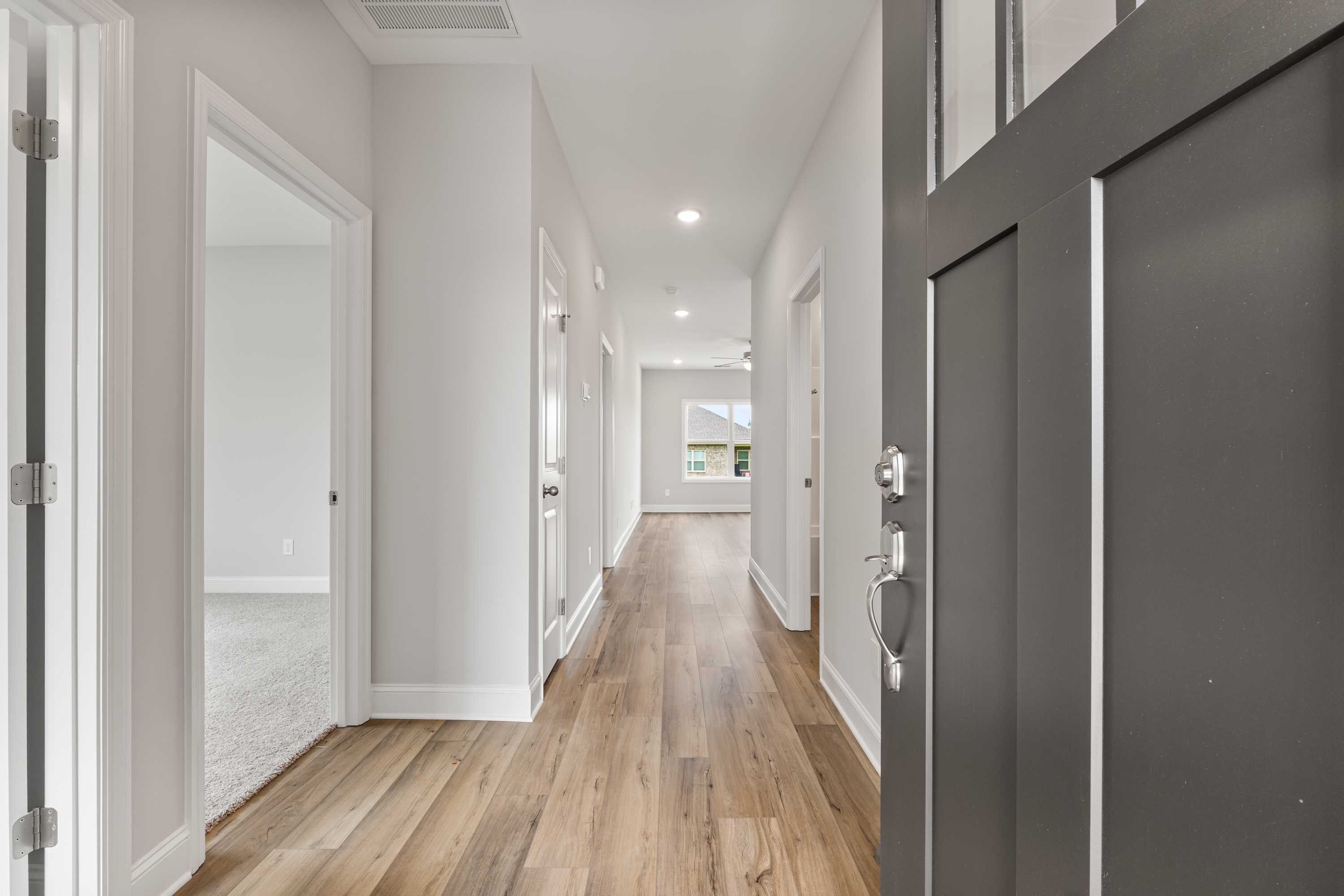 Spacious hallway in The Butler 3-bedroom home with hardwood floors, light gray walls, and dark front door