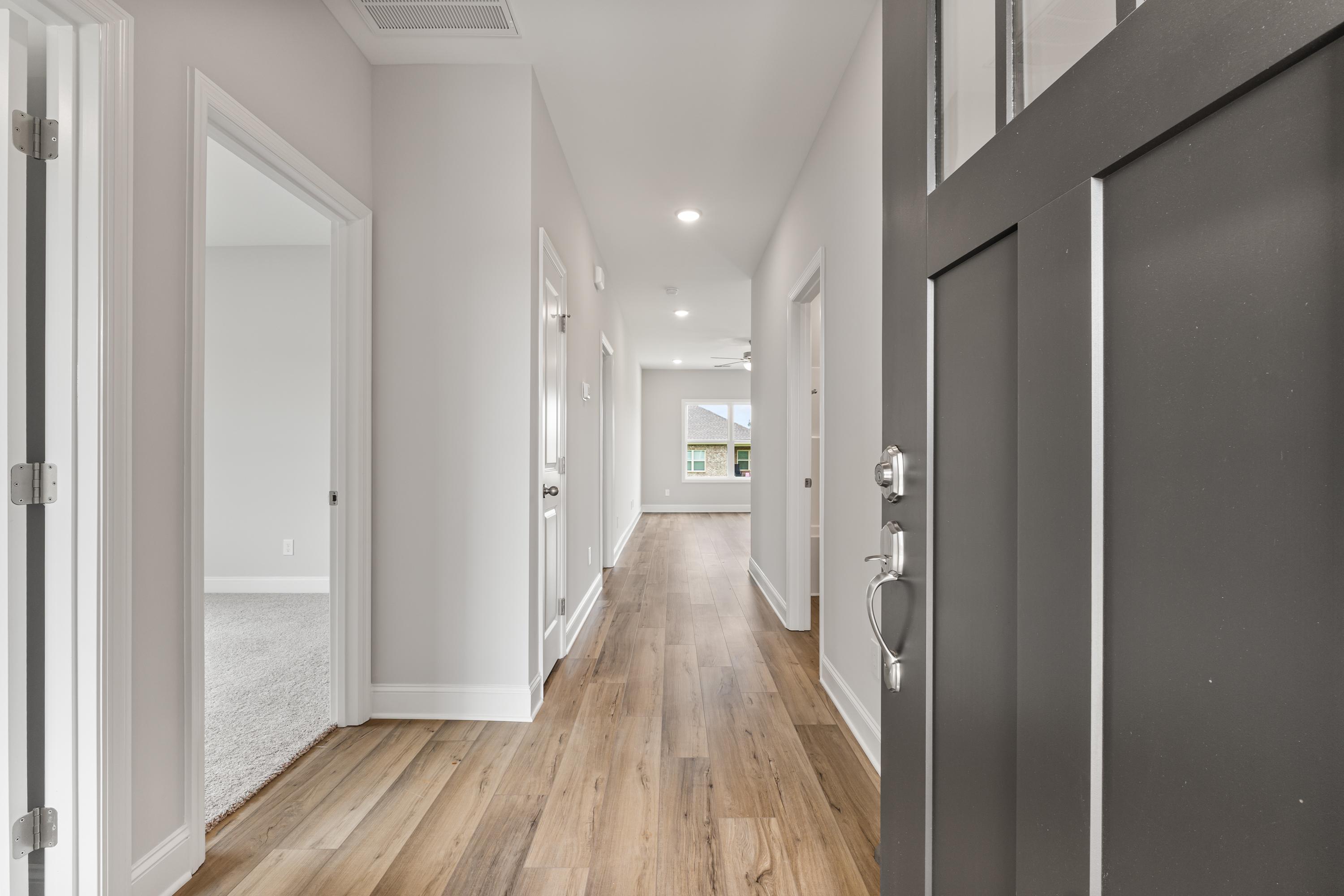Spacious hallway in The Butler 3-bedroom home with hardwood floors, light gray walls, and dark front door