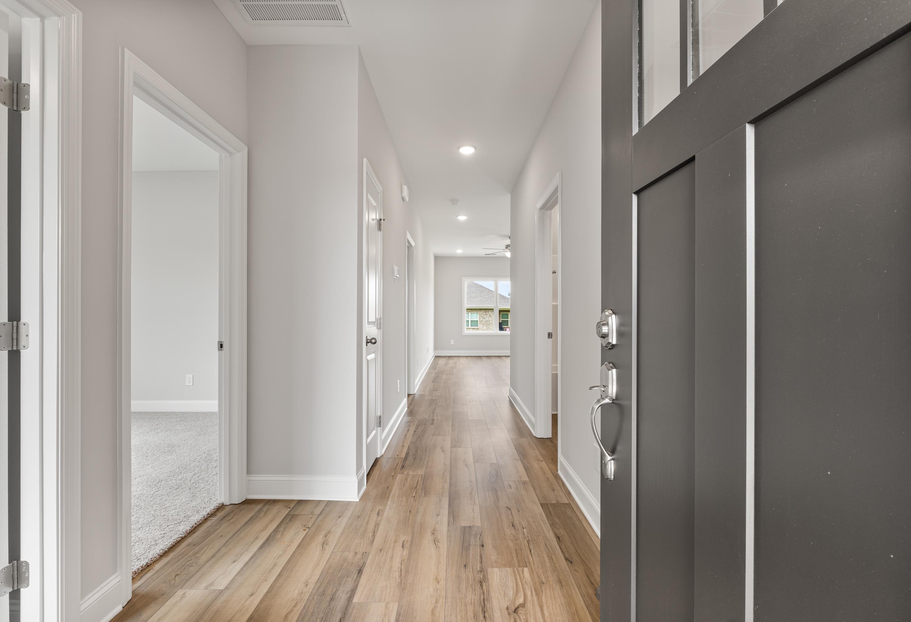 Spacious hallway in The Butler 3-bedroom home with hardwood floors, light gray walls, and dark front door