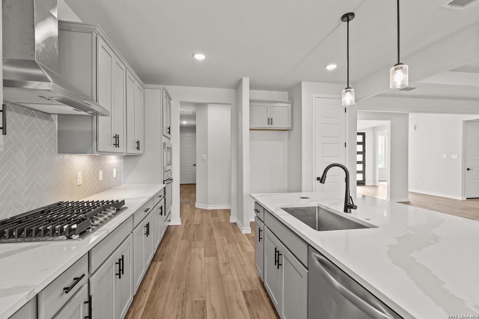 Modern kitchen with gray cabinets, quartz countertops, herringbone backsplash, and large island in Davidson Homes' The Oxford F, Castroville