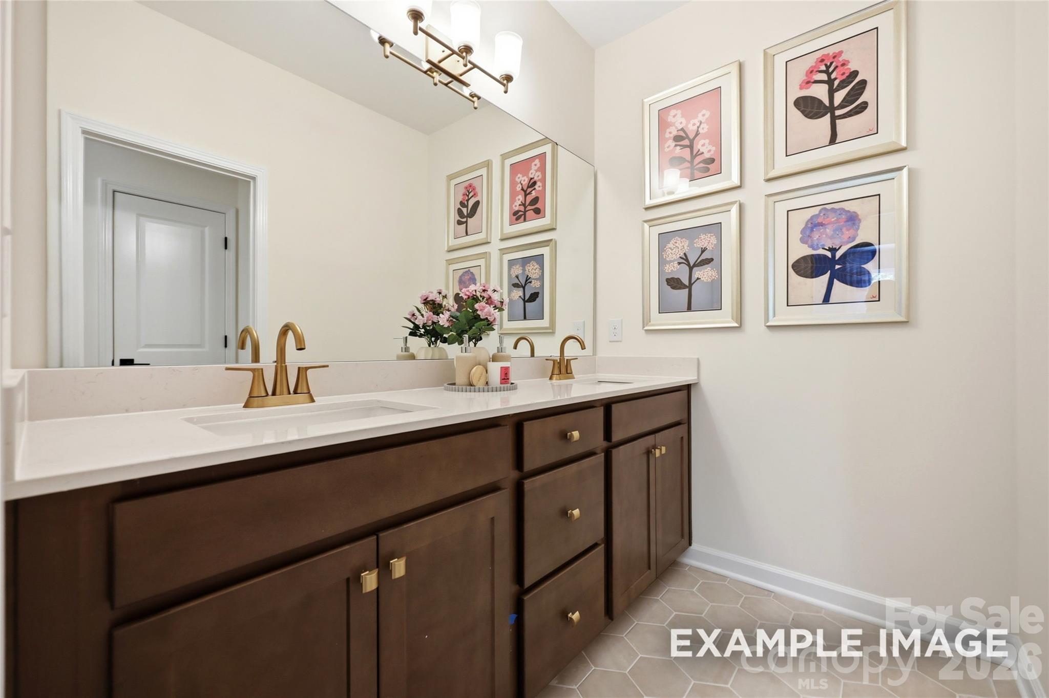Elegant dual-sink bathroom with dark wood vanity, gold fixtures, and floral gallery wall in Davidson Homes Aspen B, Windgate, Mooresville NC