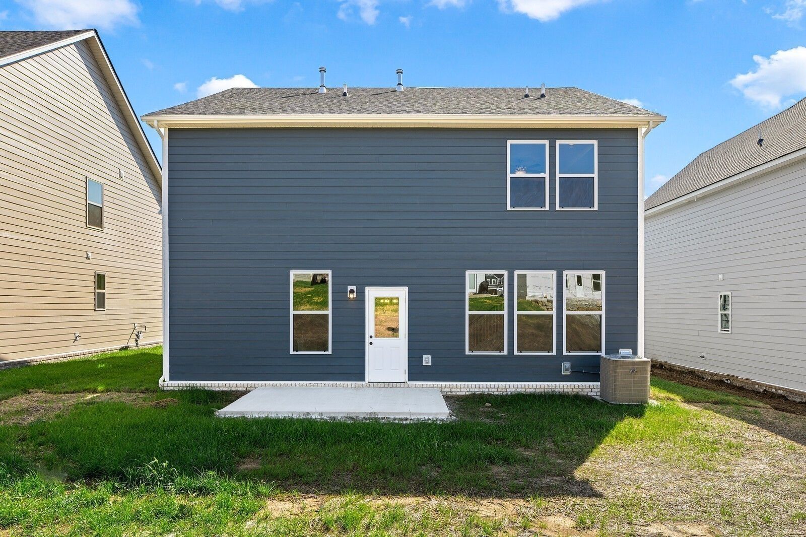Two-story navy blue home rear with large windows, white door, concrete patio, and green yard in Woods Crossing, Gallatin, Tennessee - The Logan C