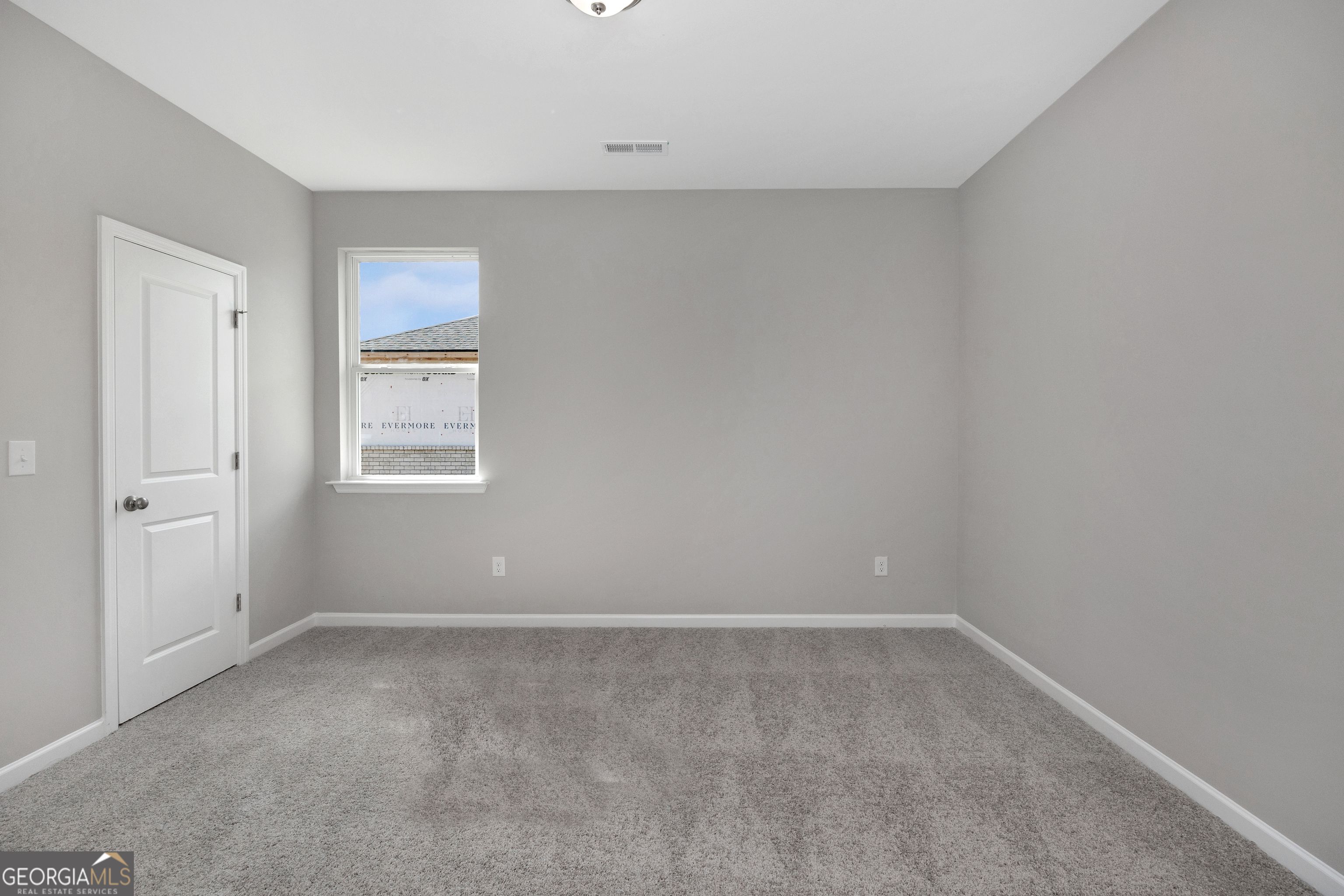 Empty secondary bedroom featuring gray walls, carpet flooring, white door, and window in The Luna 4-bedroom home by Evermore Homes, Perry, Georgia