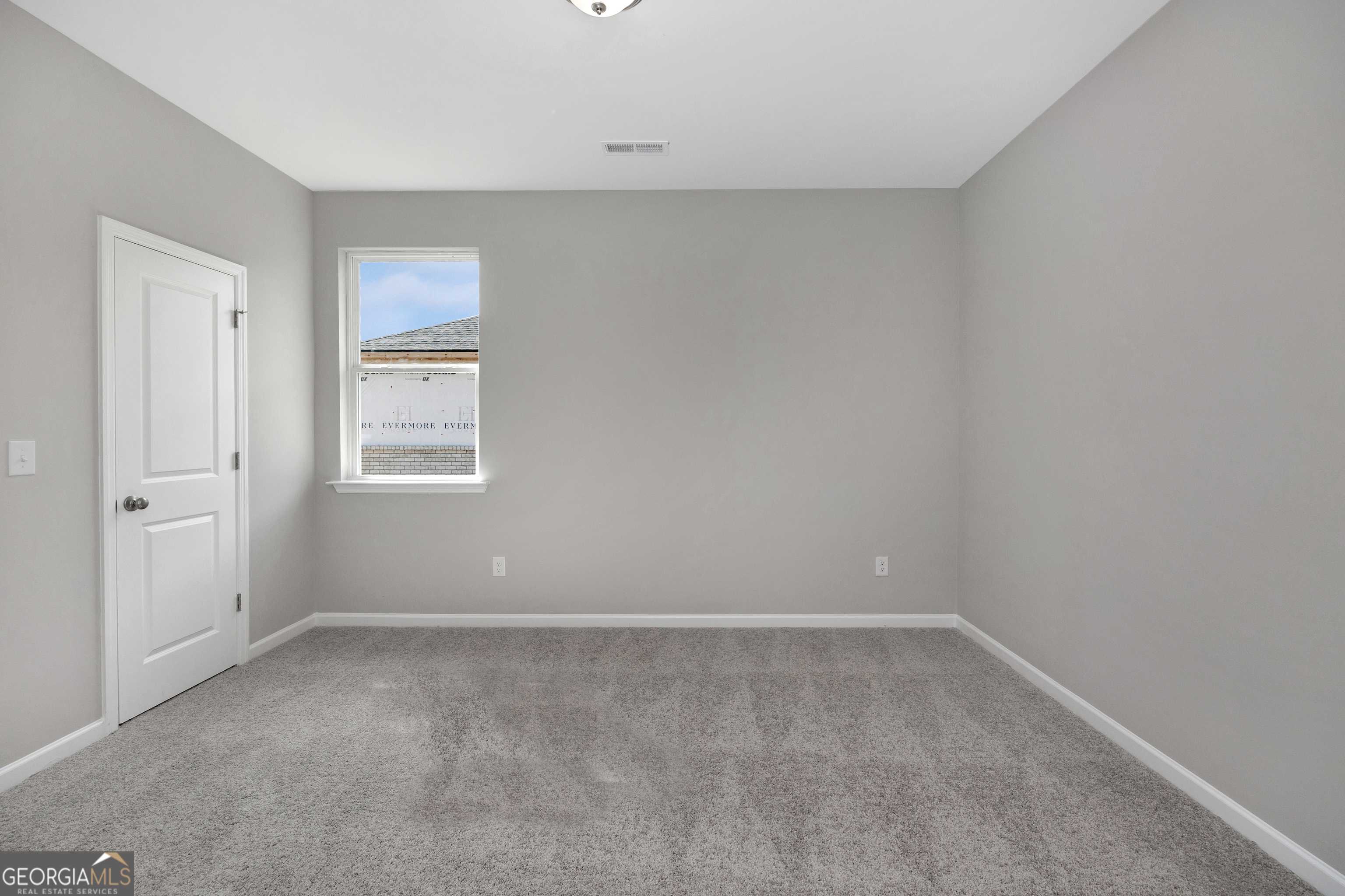 Empty secondary bedroom featuring gray walls, carpet flooring, white door, and window in The Luna 4-bedroom home by Evermore Homes, Perry, Georgia