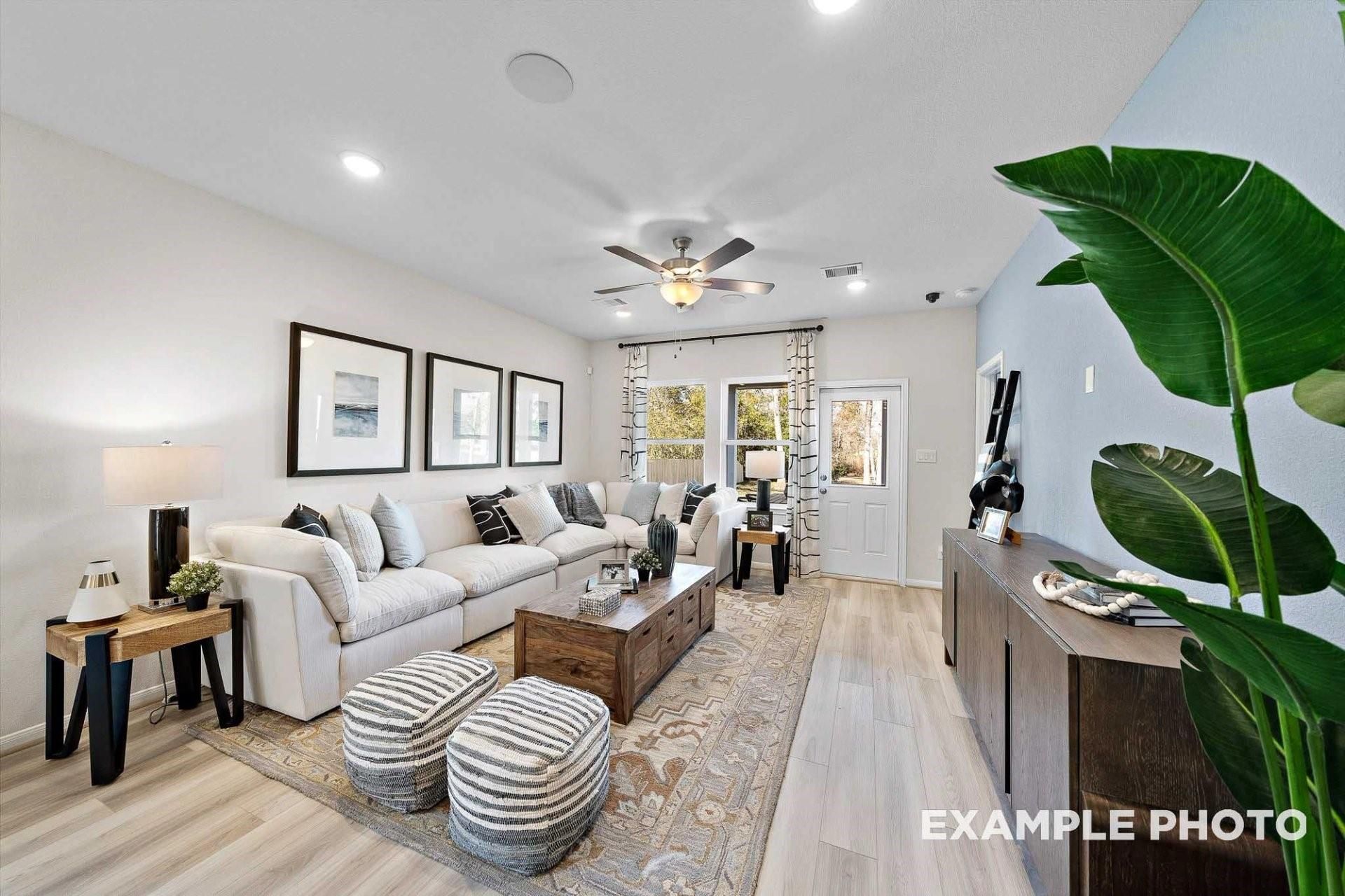 Modern living room with white L-shaped sofa, ceiling fan, hardwood floors, and potted plants in Davidson Homes The San Marcos E, Magnolia, Texas