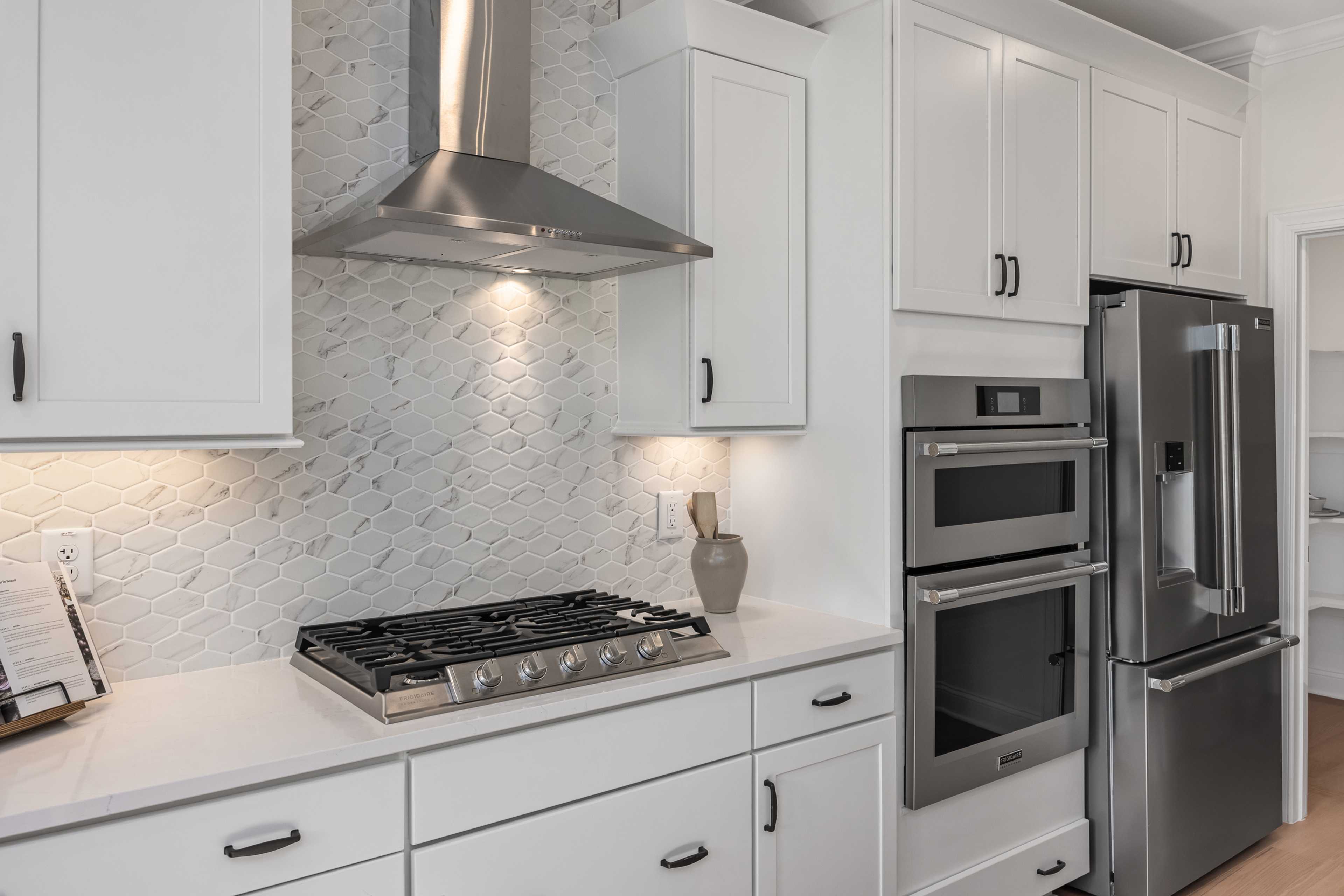 Modern kitchen at Laneridge Estates in Raleigh NC by Davidson Homes with white cabinets, stainless steel gas range, double ovens, and subway tile backsplash
