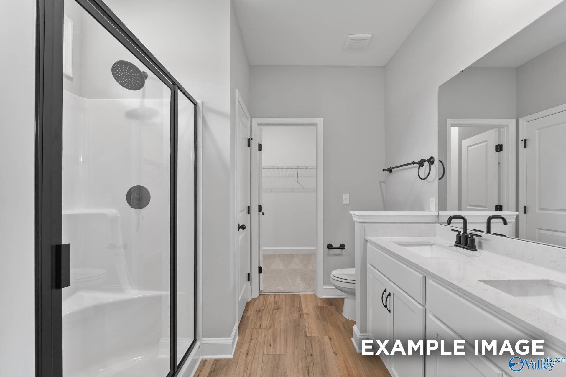 Modern master bathroom with frameless glass shower, double vanity, and hardwood floors in Davidson Homes The Asheville C, Hazel Green, AL