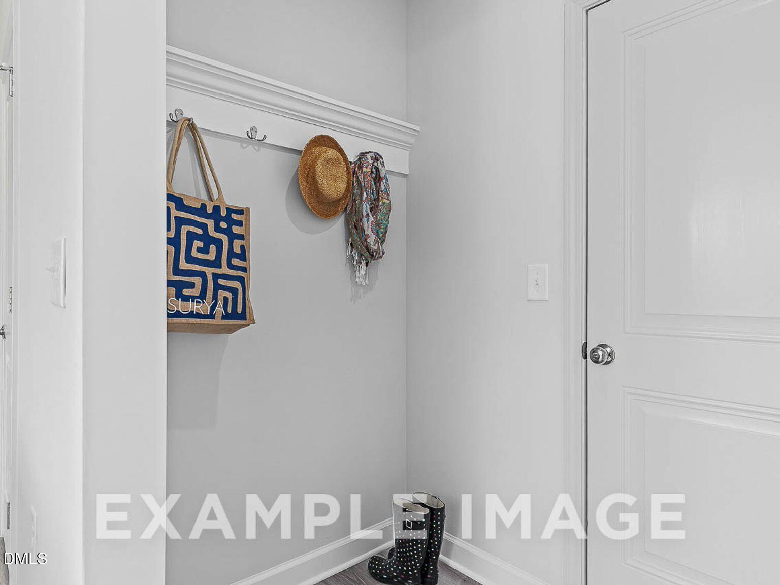 Cozy mudroom with wall hooks, blue patterned tote bag, hat, scarf, and black boots near white entry door in The Chestnut B home, Lillington NC