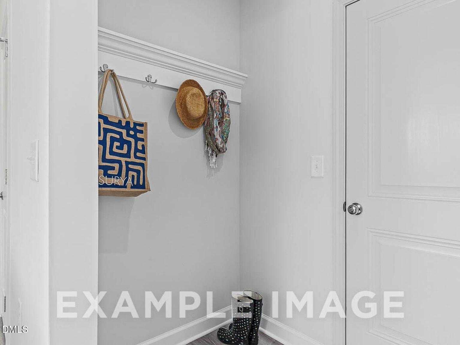 Functional mudroom with coat hooks, blue tote bag, tan hat, scarf, and black boots in Davidson Homes The Chestnut B, Lillington, NC