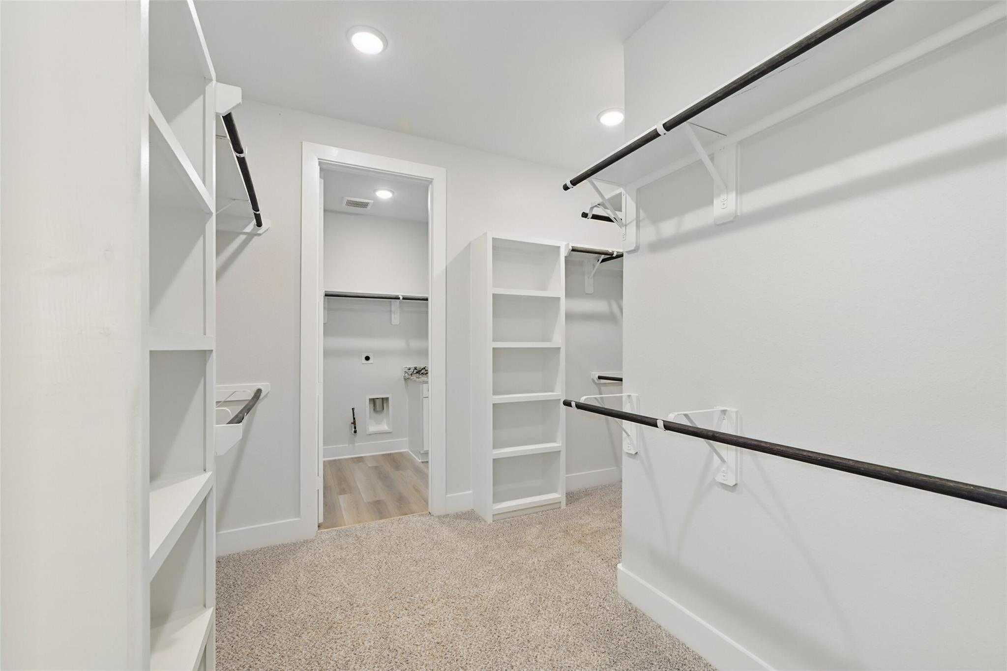 Spacious walk-in closet with white built-in shelves, hanging rods, and adjacent bathroom in Davidson Homes The Victoria C, Lago Mar, Texas City