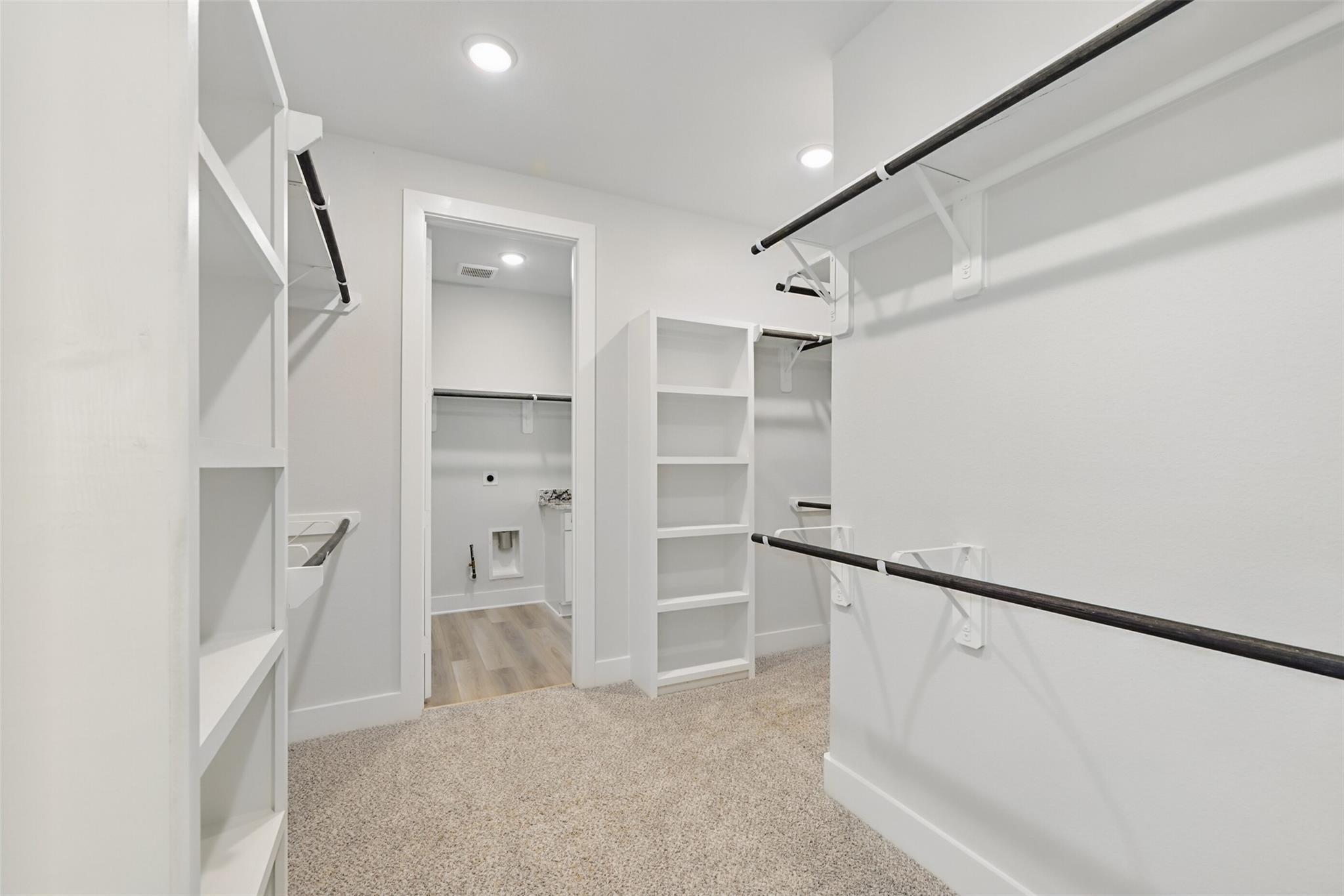 Spacious walk-in closet with white built-in shelves, hanging rods, and adjacent bath in Davidson Homes The Victoria C, Lago Mar, Texas City