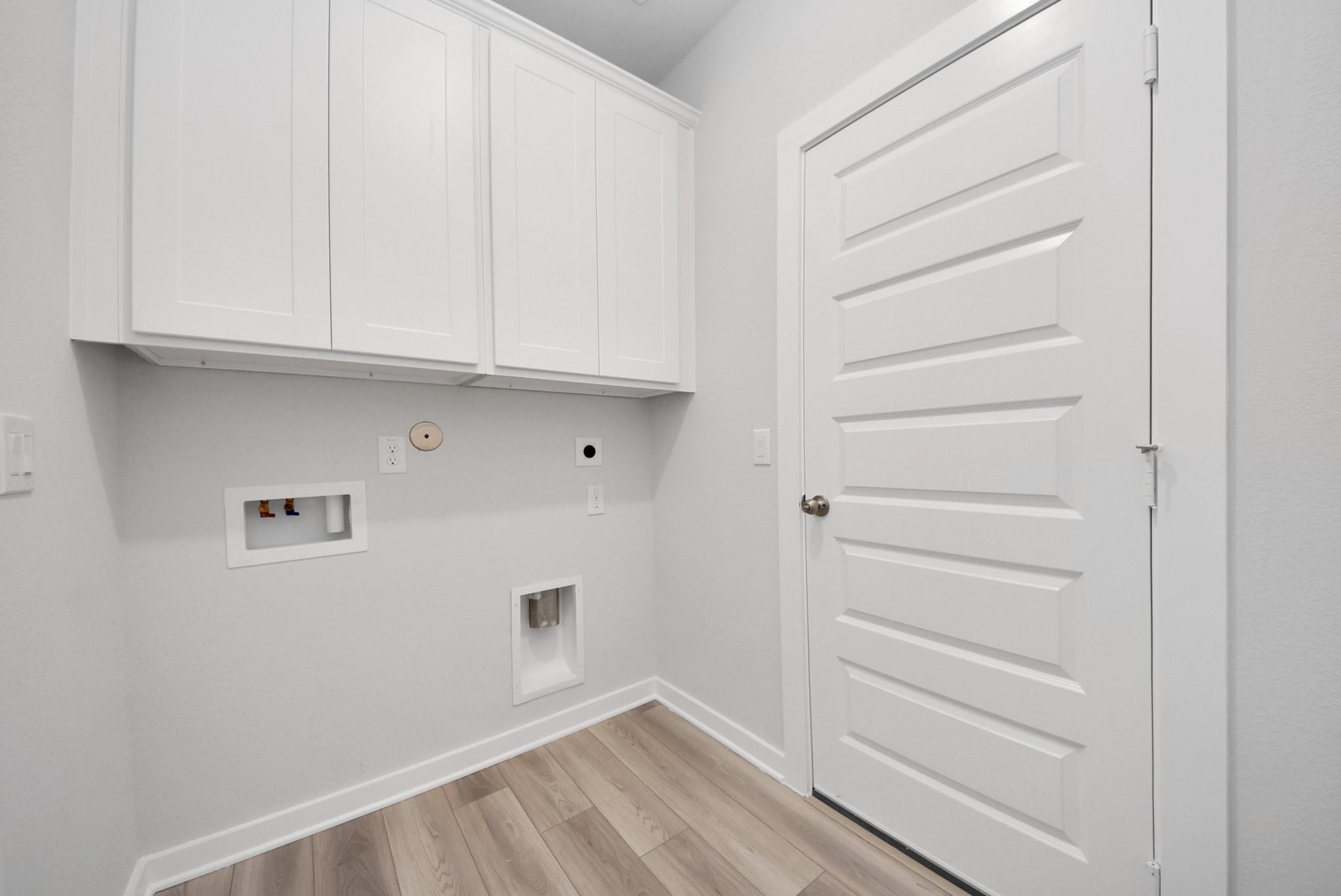 Modern laundry room with white cabinets and wood-style flooring in The Sabine E floor plan at Windmill Estates, Magnolia.