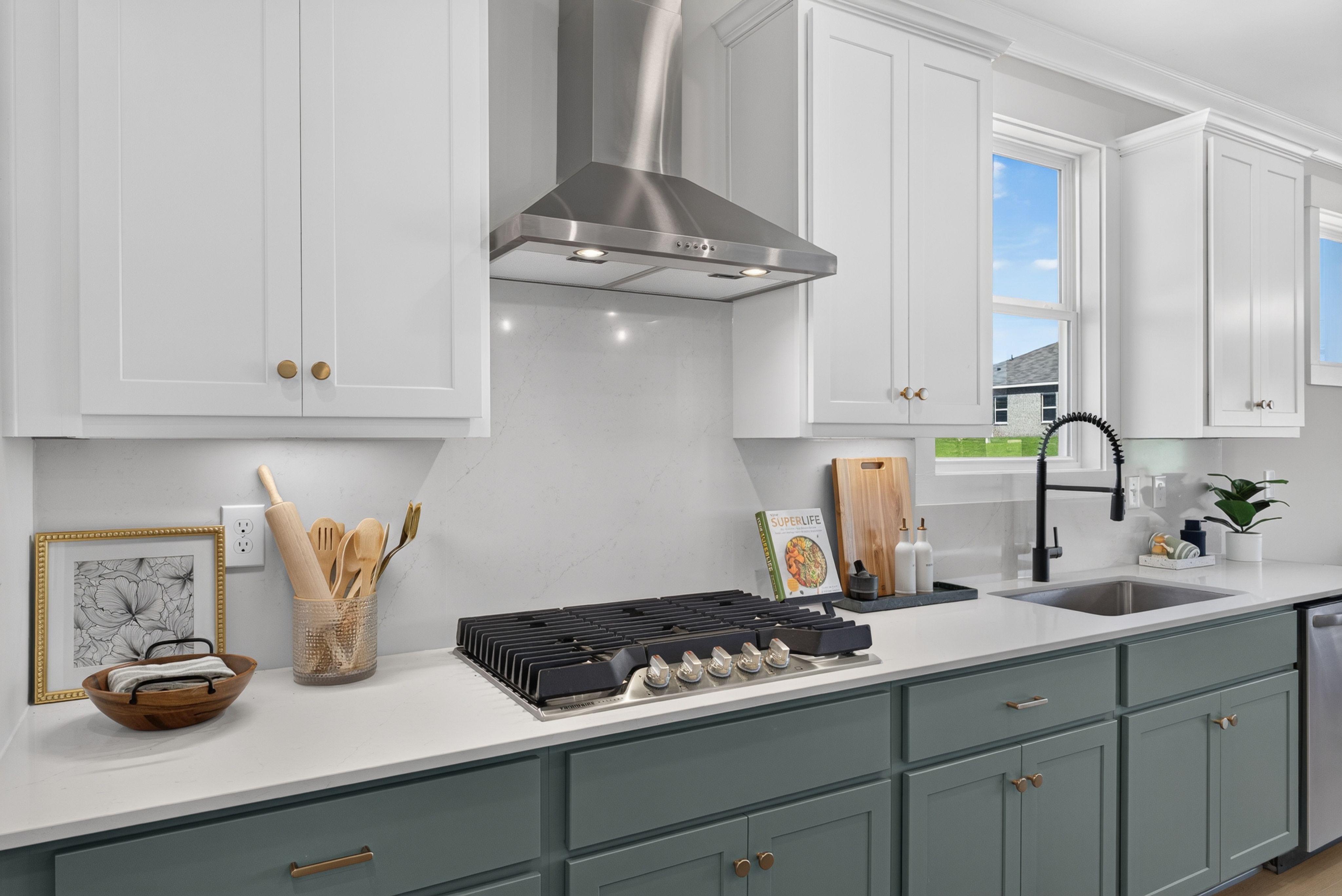 Modern kitchen at Evergreen Mill in Madison, Alabama with white cabinets, gas cooktop, and stainless steel range hood by Davidson Homes