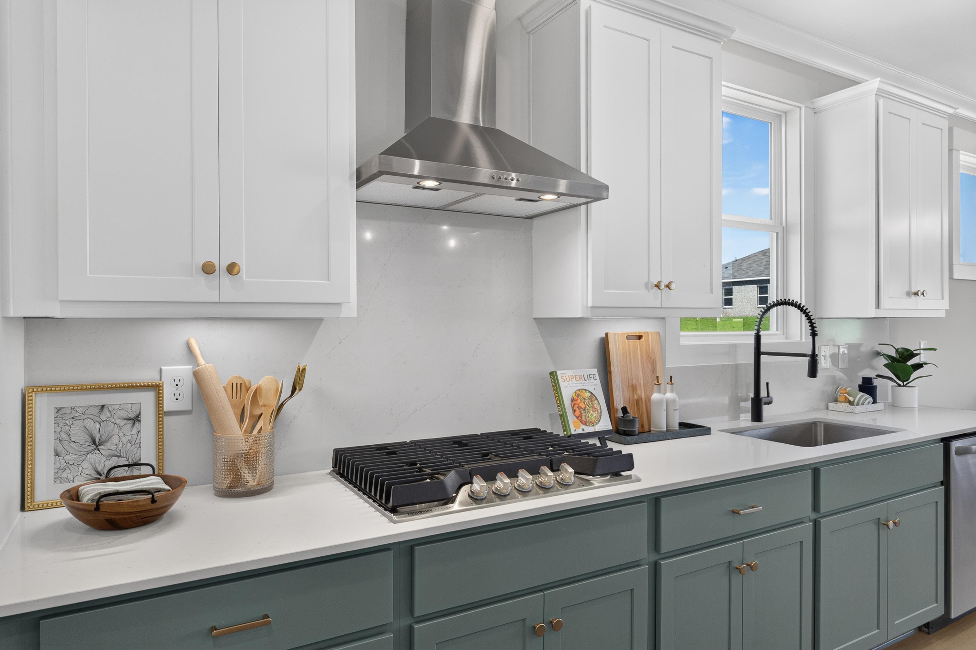 Modern kitchen at Evergreen Mill in Madison, Alabama with white cabinets, gas cooktop, and stainless steel range hood by Davidson Homes