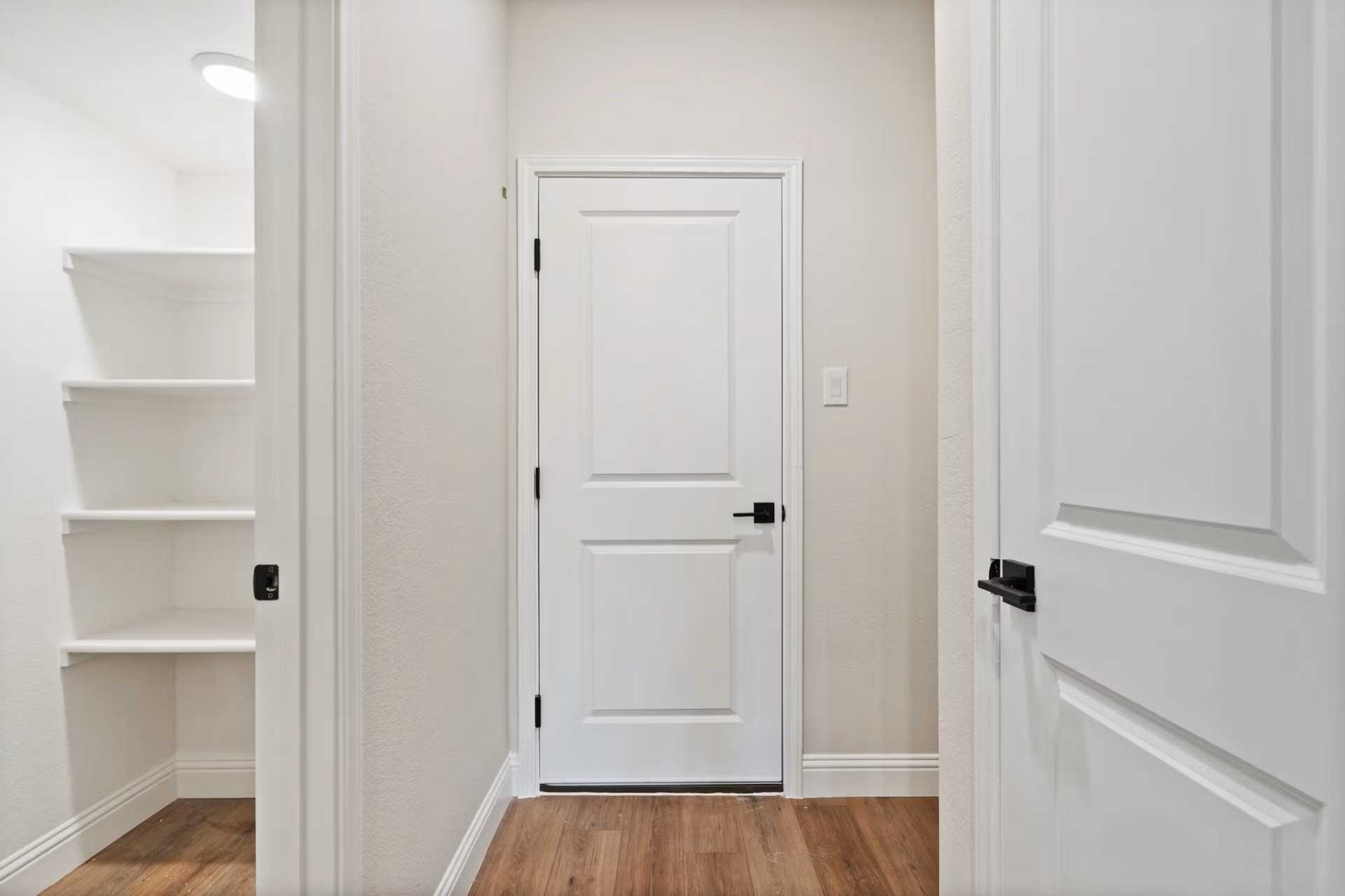 Bright hallway with open white pantry shelves, white doors, and hardwood floors in Davidson Homes The Wake D, Wylie, Texas