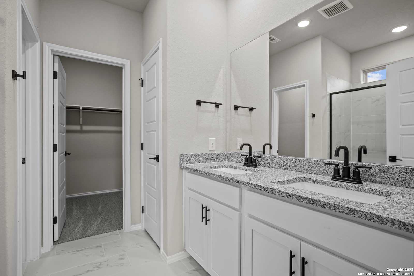 Modern master bathroom featuring double vanity with granite countertop and adjacent walk-in closet in Davidson Homes Asheville E, Converse, Texas