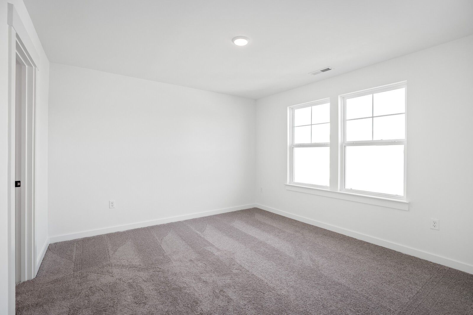 Bright empty bedroom with white walls, large double windows, and neutral carpet in Davidson Homes The Willow C, Gallatin, TN