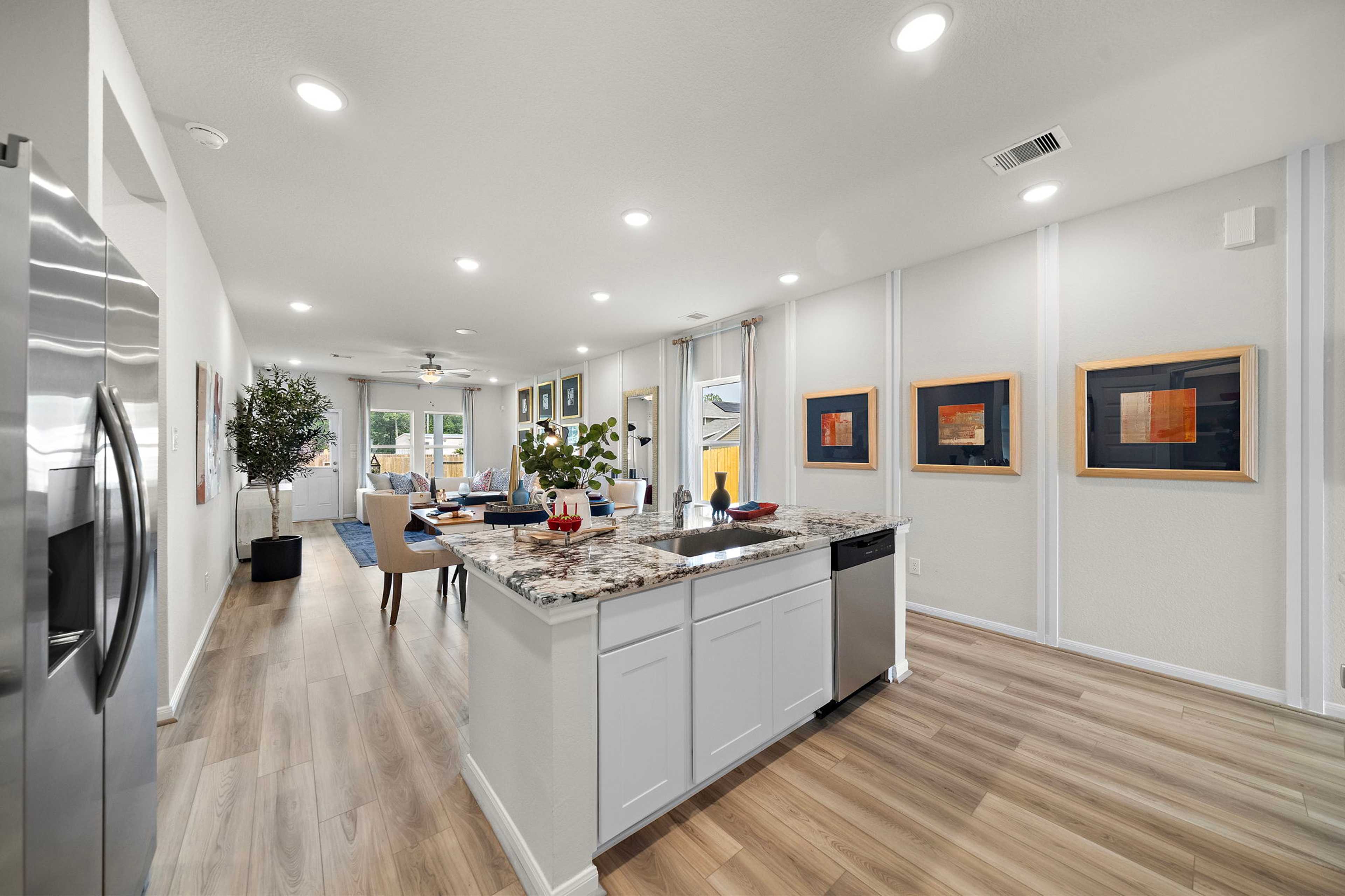 Spacious open-concept kitchen dining area in Liberty Estates Cleveland Texas home with white cabinets granite island hardwood floors and modern art