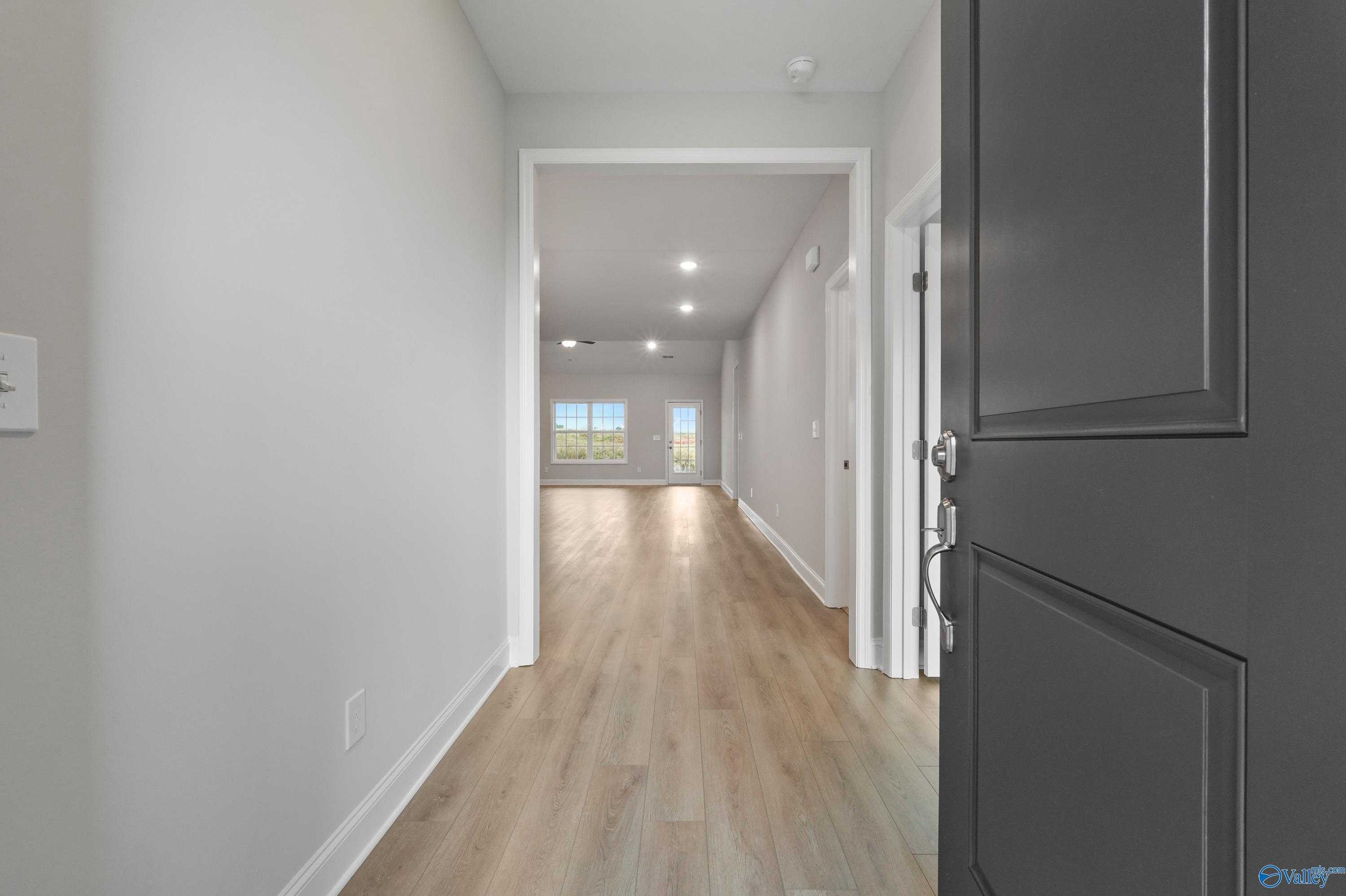 Bright hallway with light wood floors, gray walls, and open doorway to sunlit room in Davidson Homes The Lanier, Harvest AL