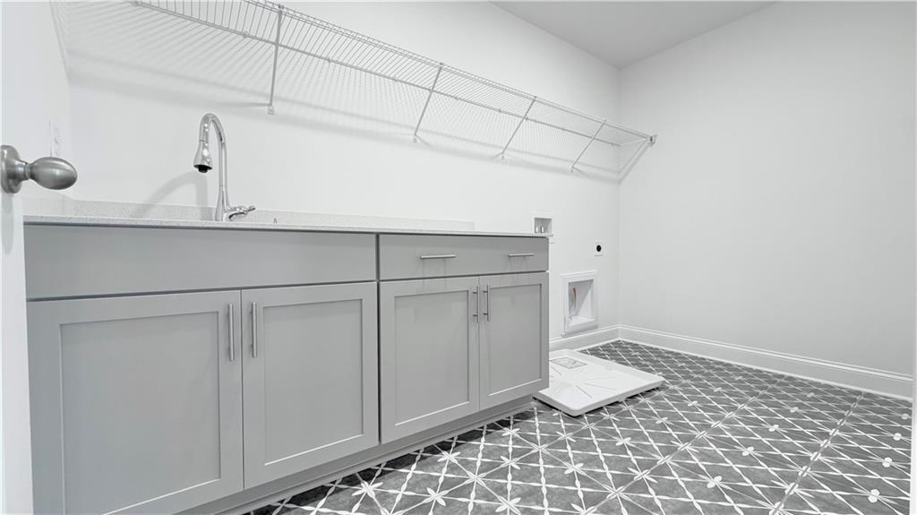 Laundry room with gray cabinets, utility sink, and patterned tile flooring in The Hickory C home at Wehunt Meadows, Hoschton