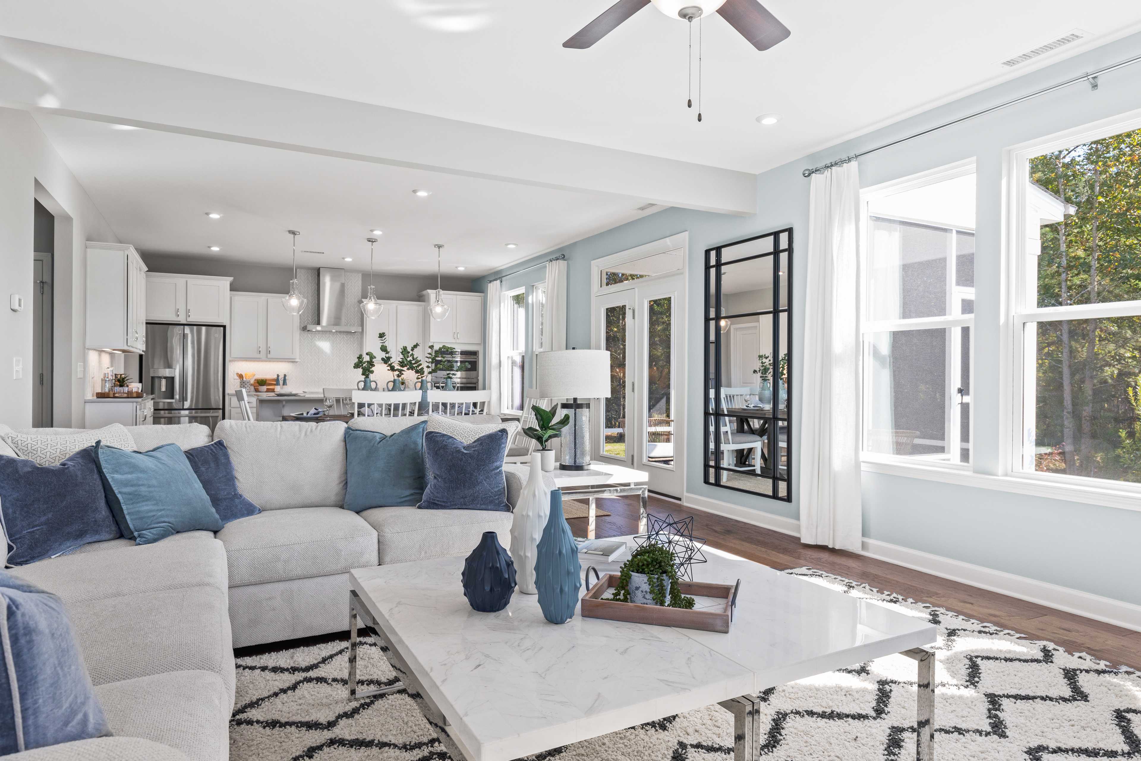 Spacious open-concept living room and kitchen at Enclave at Belmont in Belmont NC with blue sectional sofa, hardwood floors, and large windows