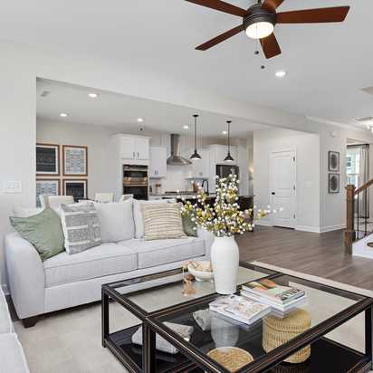 Spacious modern living room with white walls, open white kitchen, light gray sofa with green pillows, glass coffee table, har