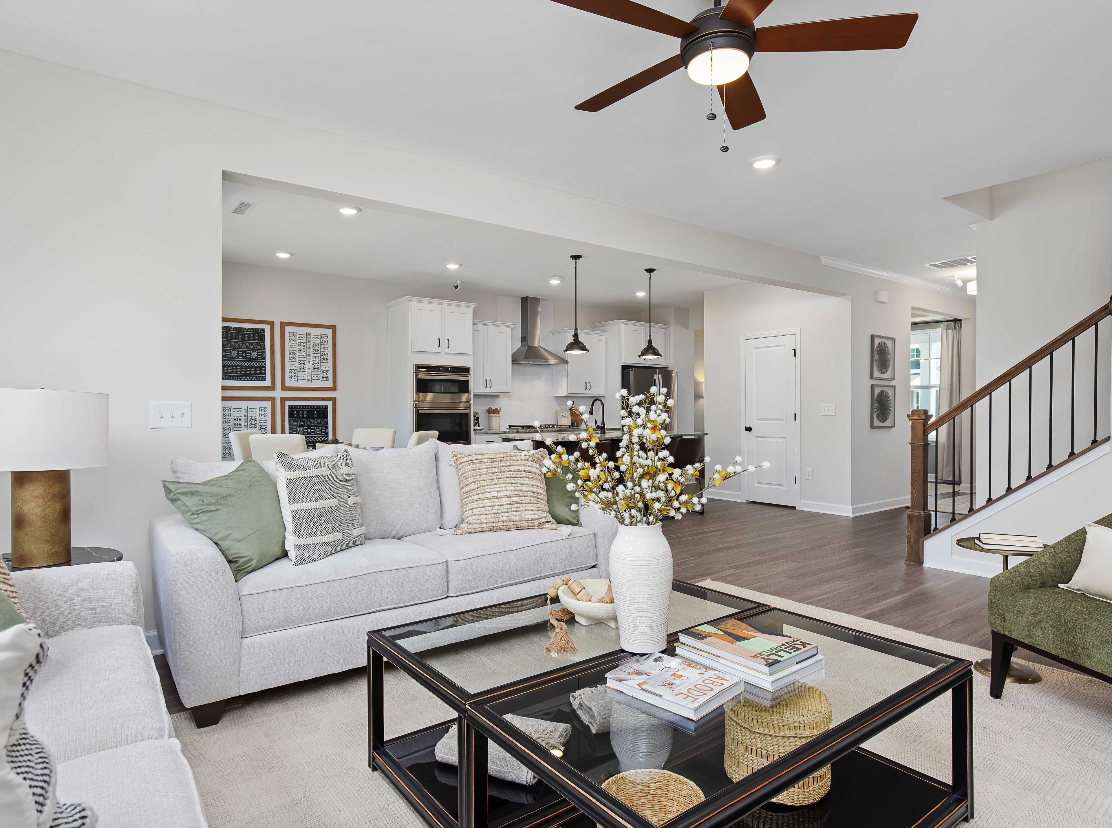 Spacious modern living room with white walls, open white kitchen, light gray sofa with green pillows, glass coffee table, har
