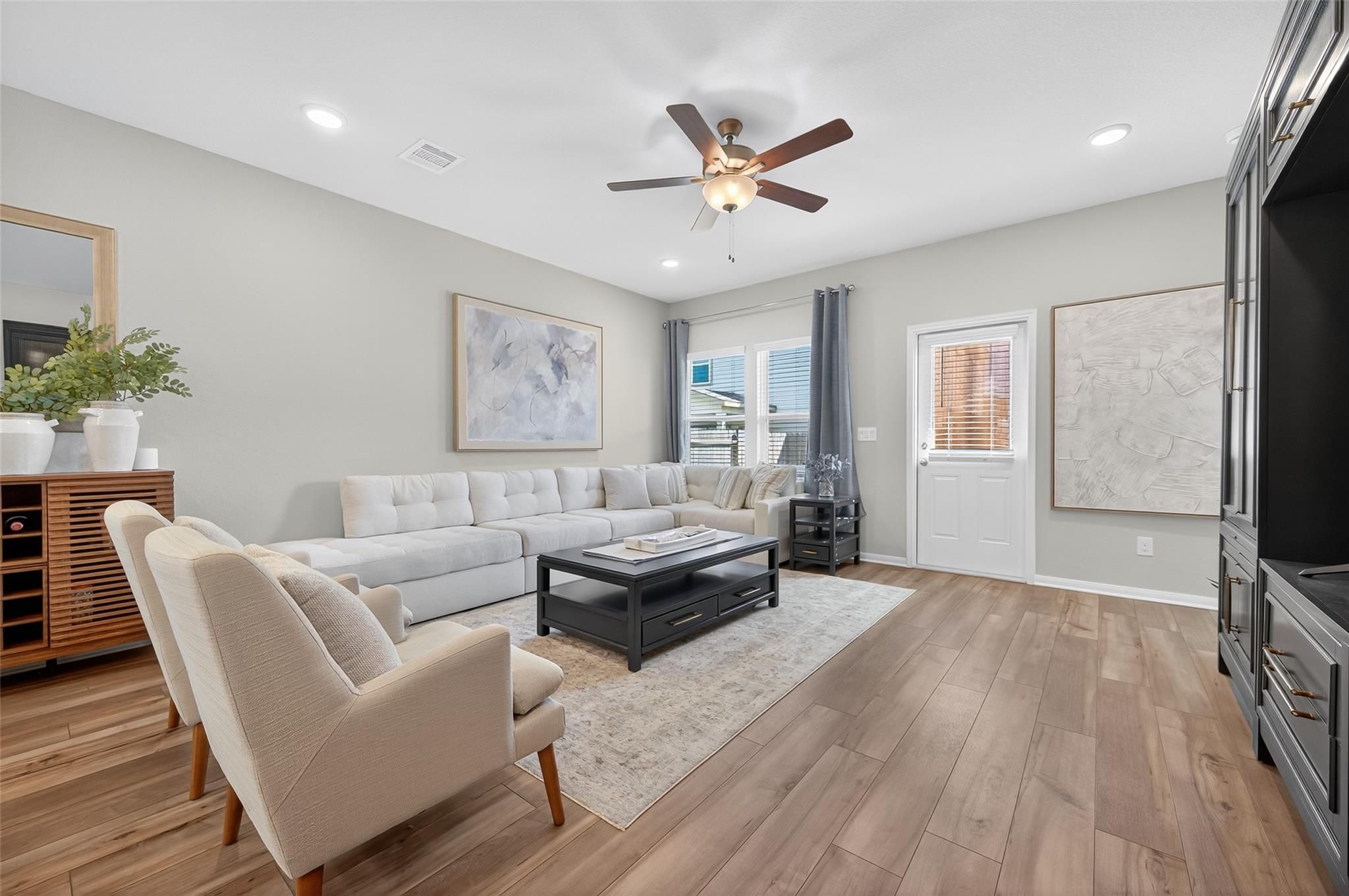 Cozy living room with L-shaped sofa, ceiling fan, sliding doors, and modern cabinets in Davidson Homes The Brazos E, Magnolia, Texas