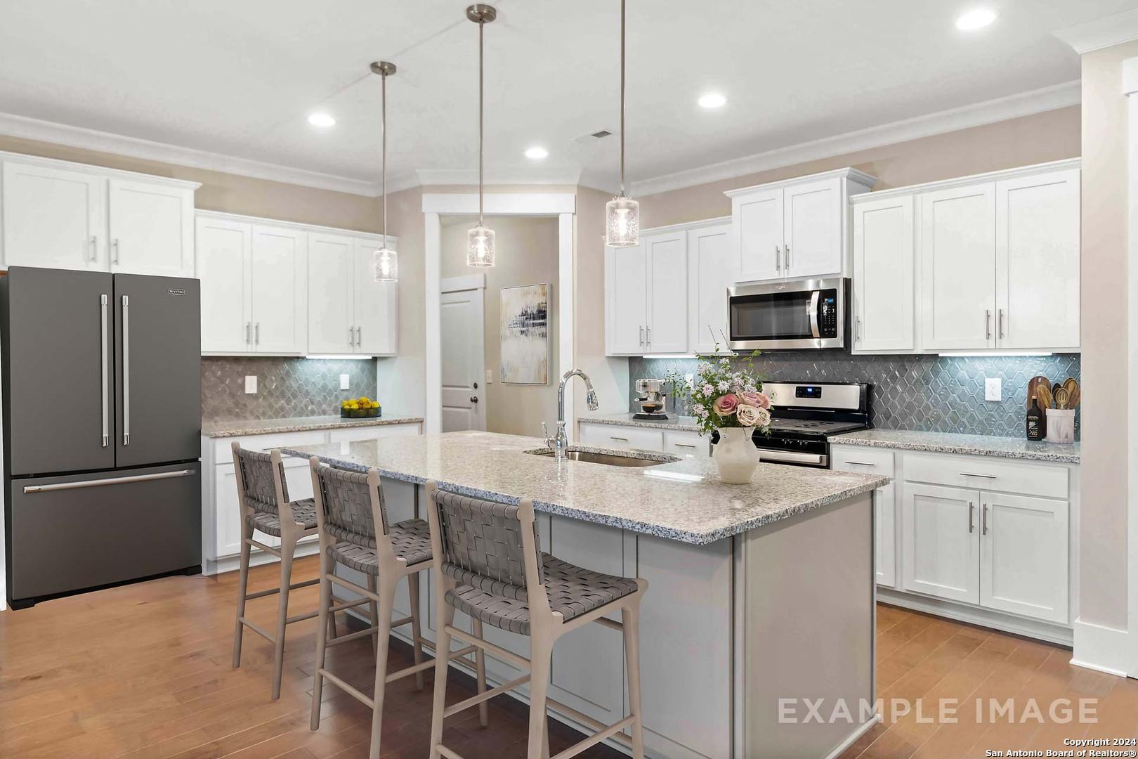 Modern white kitchen with granite island, stainless appliances, pendant lights in The Lanier H by Davidson Homes, Ladera, San Antonio