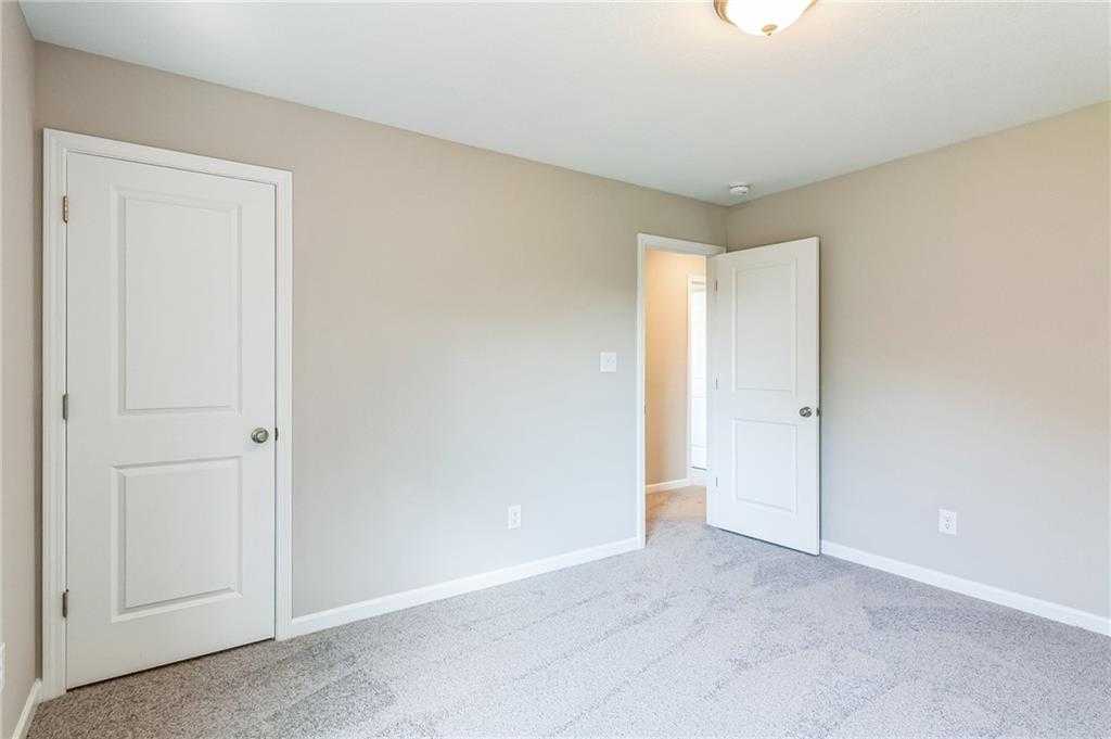 Bright secondary bedroom with beige walls, white doors, and gray carpet in Evermore Homes The Stella, Ivy Glen, Perry, Georgia