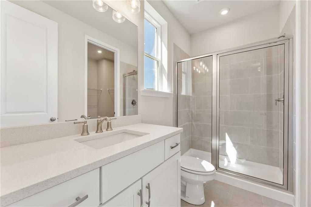 Elegant master bathroom with white quartz vanity, frameless glass shower, and natural light in Davidson Homes The Danbury E, Buford, Georgia