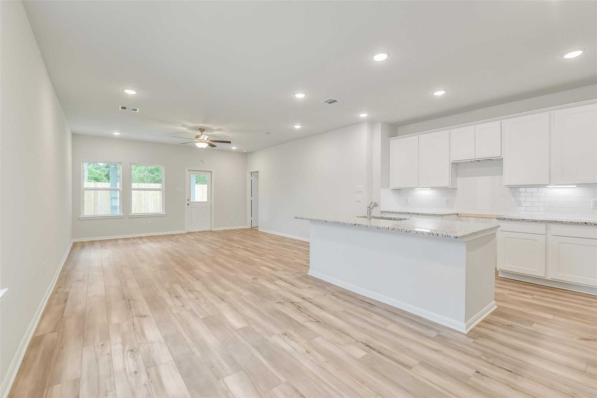Modern open-concept kitchen with white cabinets, granite island, hardwood floors in Davidson Homes The Brazos F, Conroe, Texas