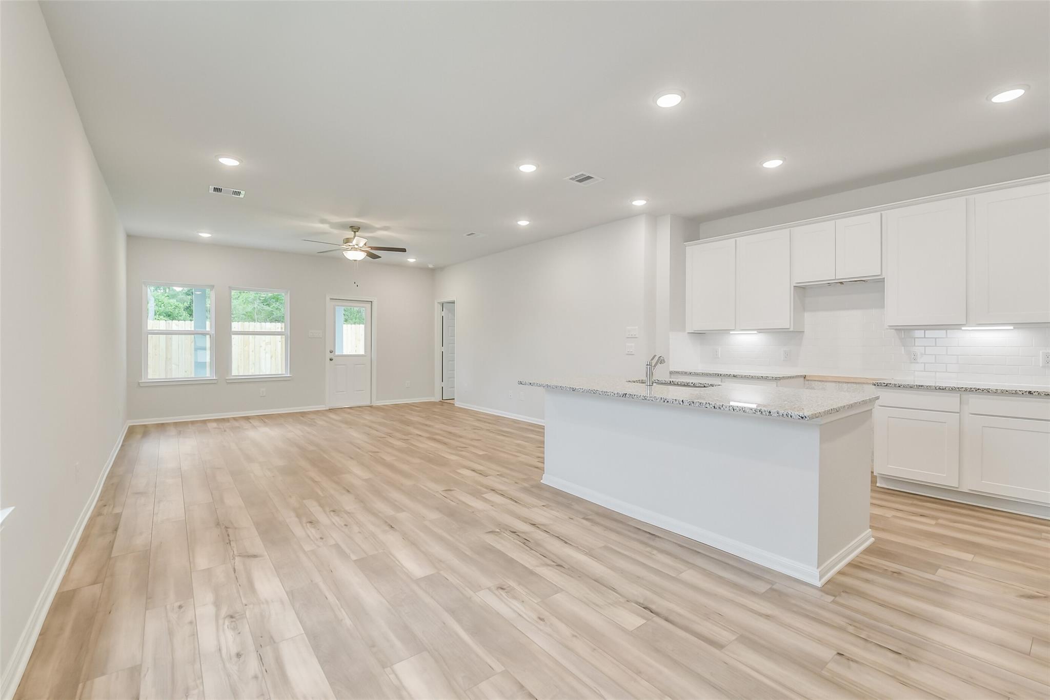 Modern open-concept kitchen with white cabinets, granite island, hardwood floors in Davidson Homes The Brazos F, Conroe, Texas