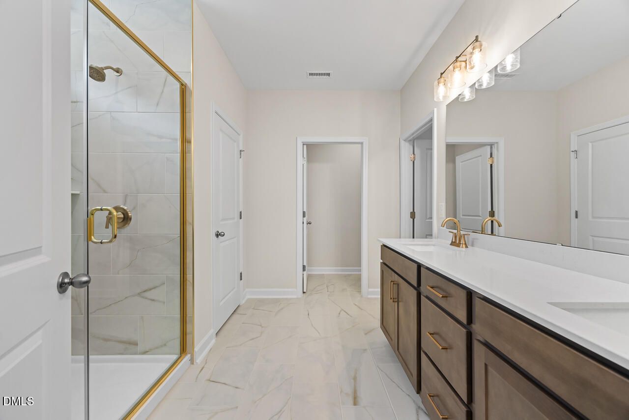Elegant primary bathroom with marble tile walk-in shower, gold fixtures, and double vanity in Davidson Homes' The Birch II C, Wake Forest, NC