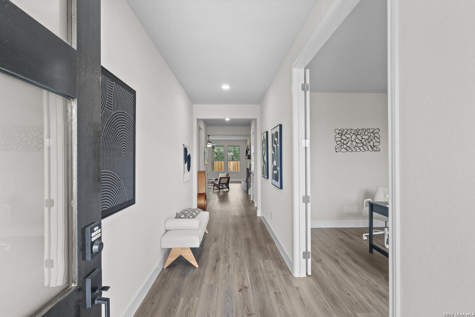 Elegant entry hallway with hardwood floors, bench seating, and abstract wall art in Davidson Homes The Belmont G, Castroville, Texas