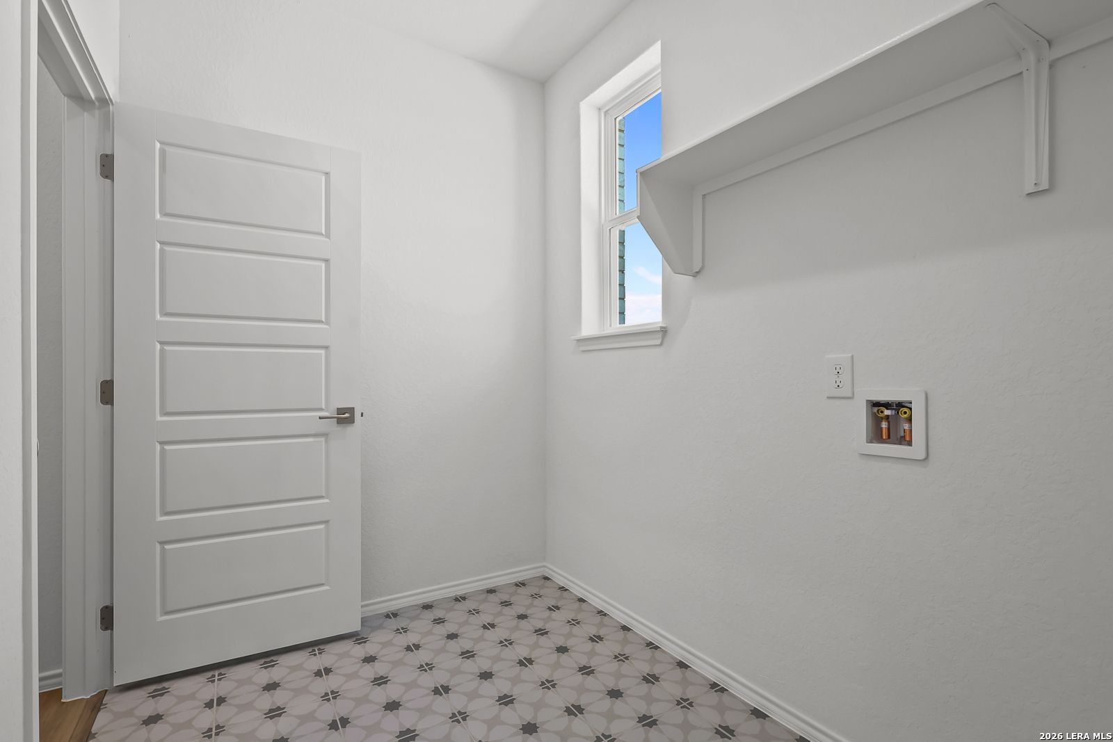 Bright laundry room with white doors, built-in shelves, window, and patterned tile floor in Davidson Homes Sequoia B, San Antonio TX
