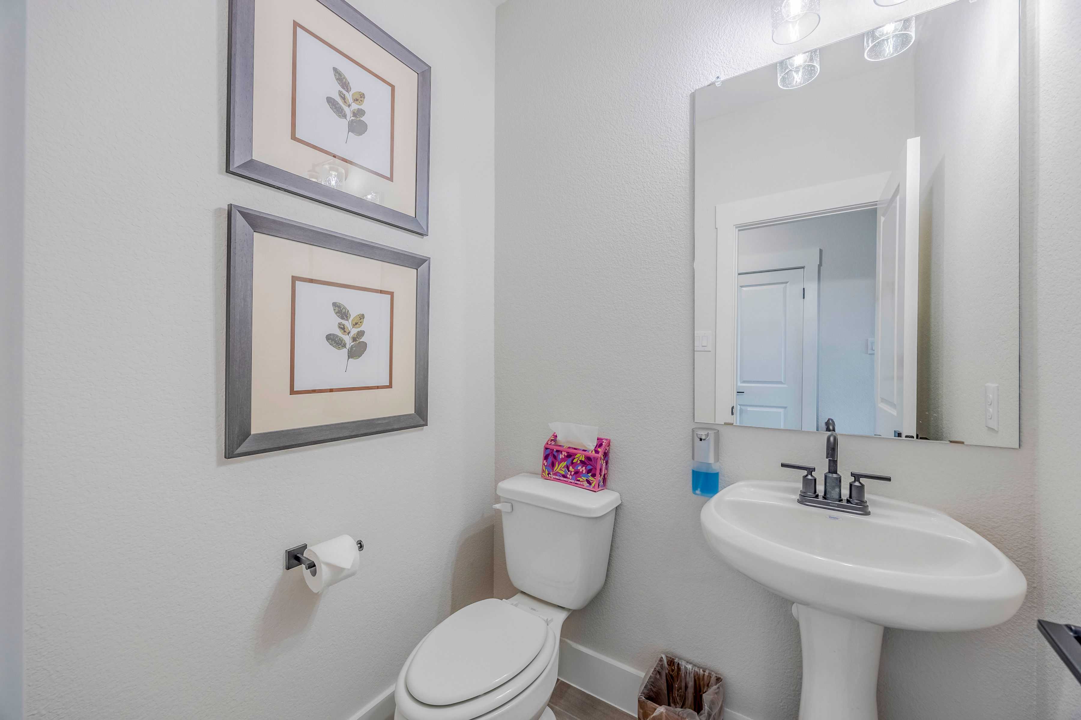 Cozy powder room in The Rockford home with white pedestal sink, toilet, framed leaf art, and soft lighting