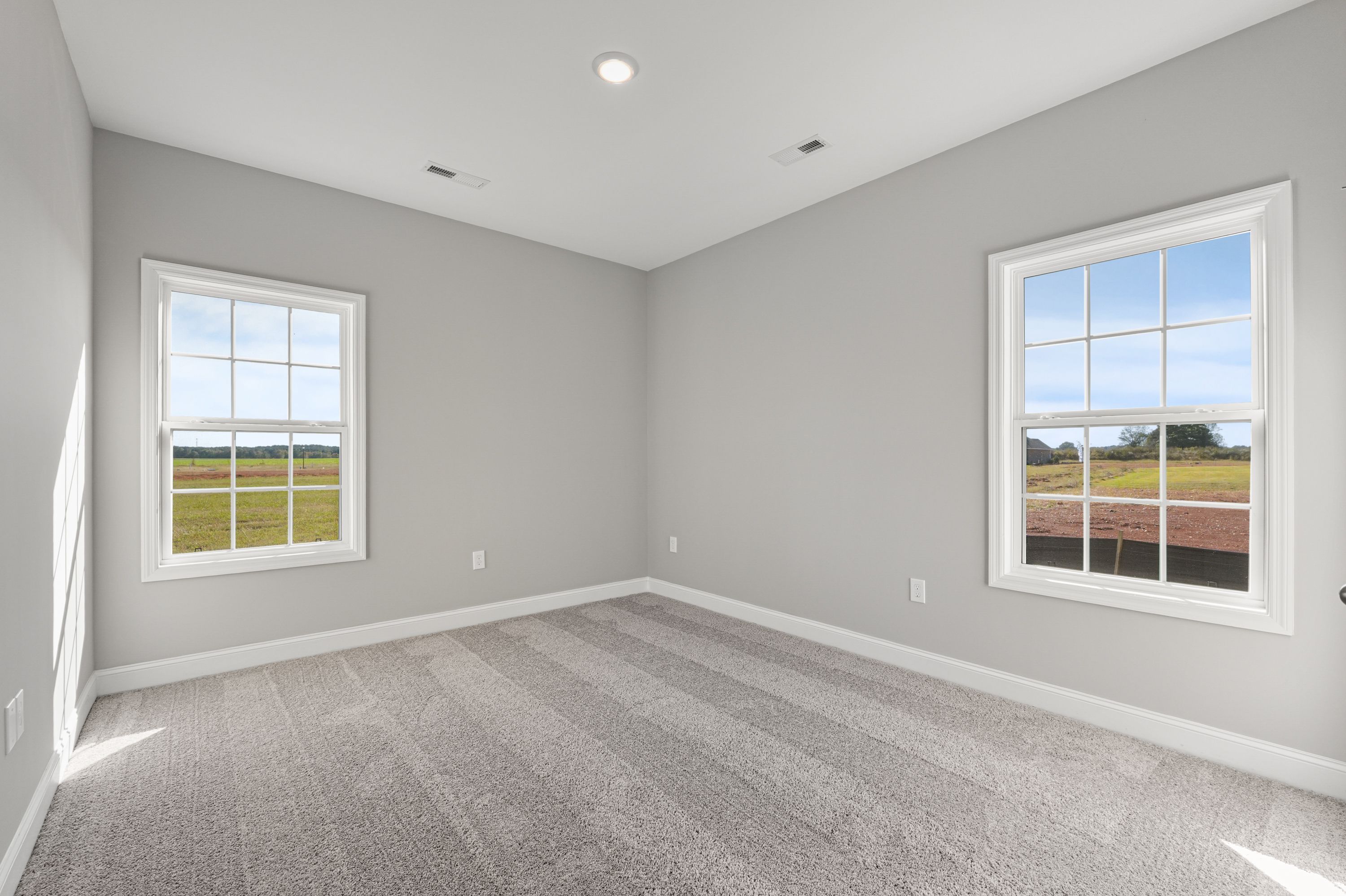 Bright secondary bedroom in The Valencia by Davidson Homes, gray walls, carpet flooring, large windows with rural field views
