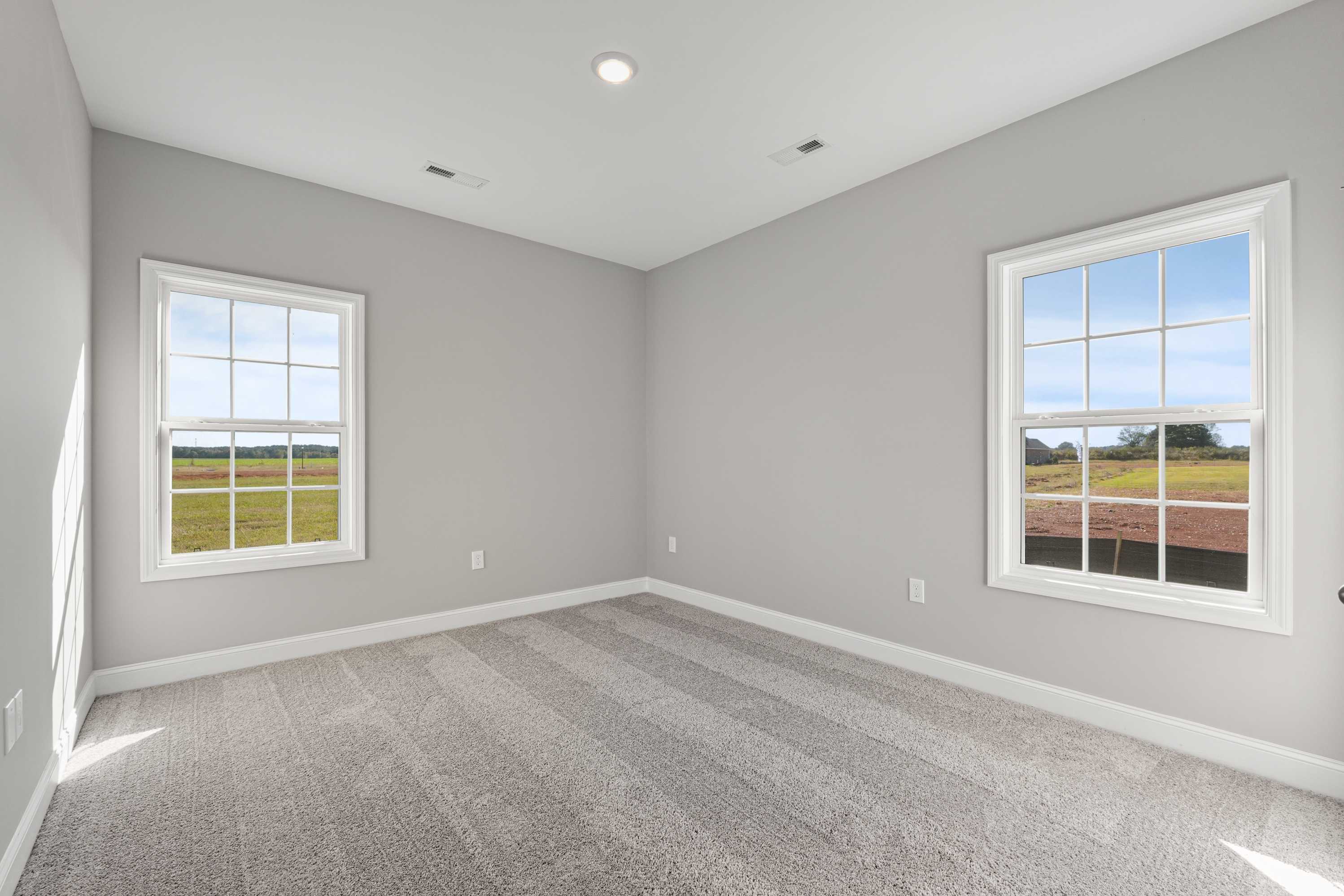 Bright secondary bedroom in The Valencia by Davidson Homes, gray walls, carpet flooring, large windows with rural field views