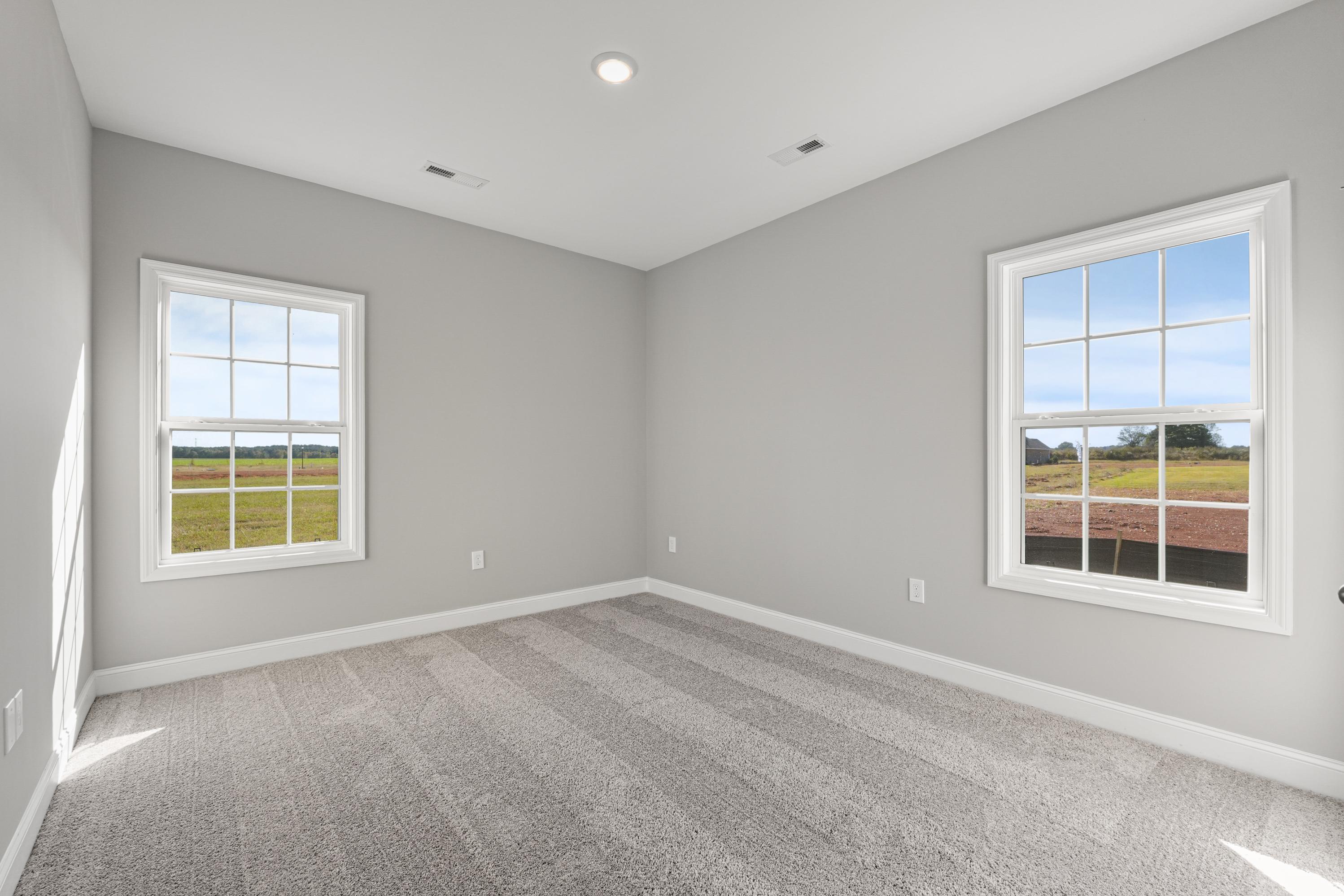 Bright secondary bedroom in The Valencia by Davidson Homes, gray walls, carpet flooring, large windows with rural field views