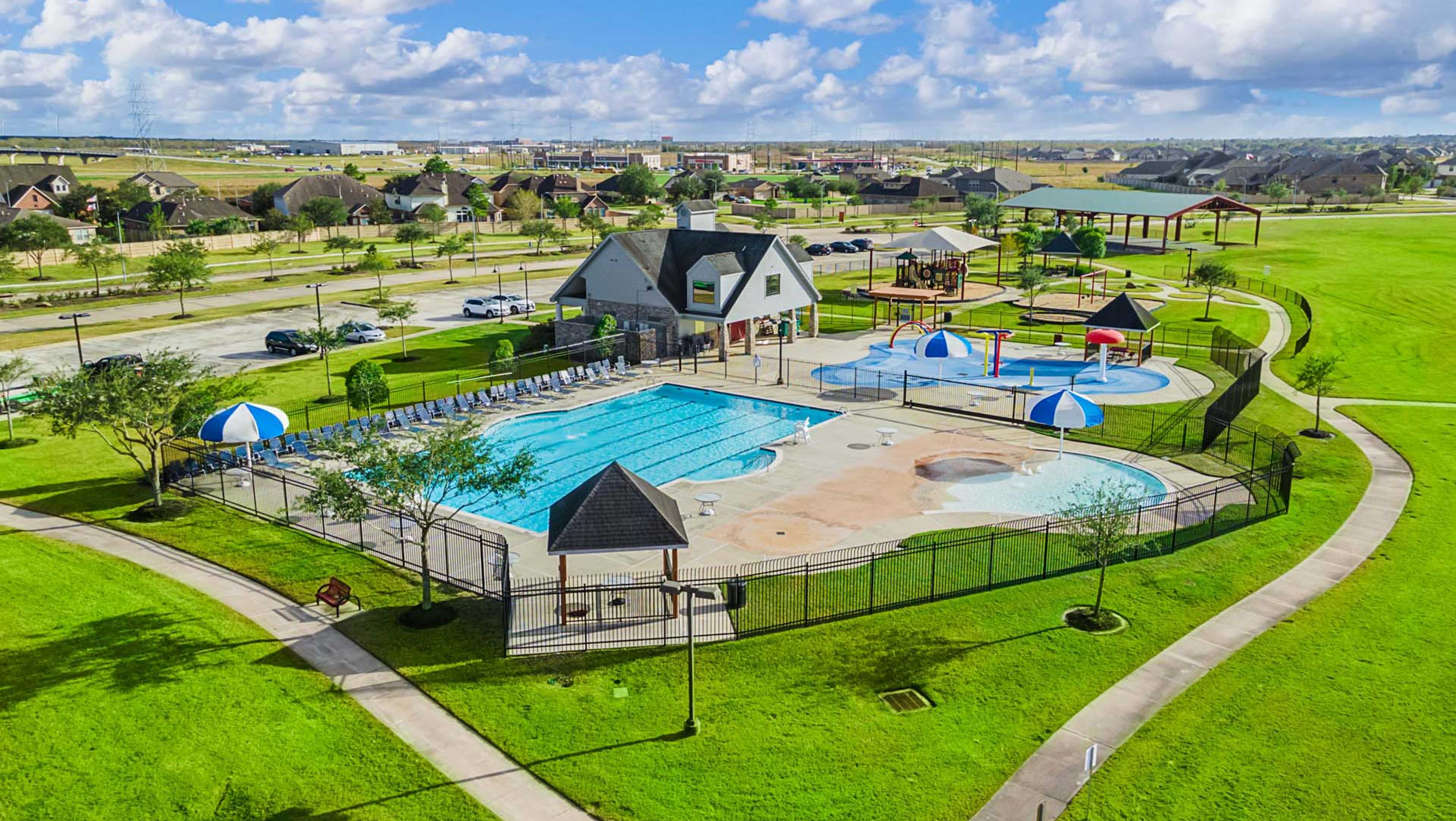 Aerial view of Sierra Vista community pool featuring clubhouse, playground, lounge chairs, umbrellas, and lush green lawns in Davidson Homes neighborhood