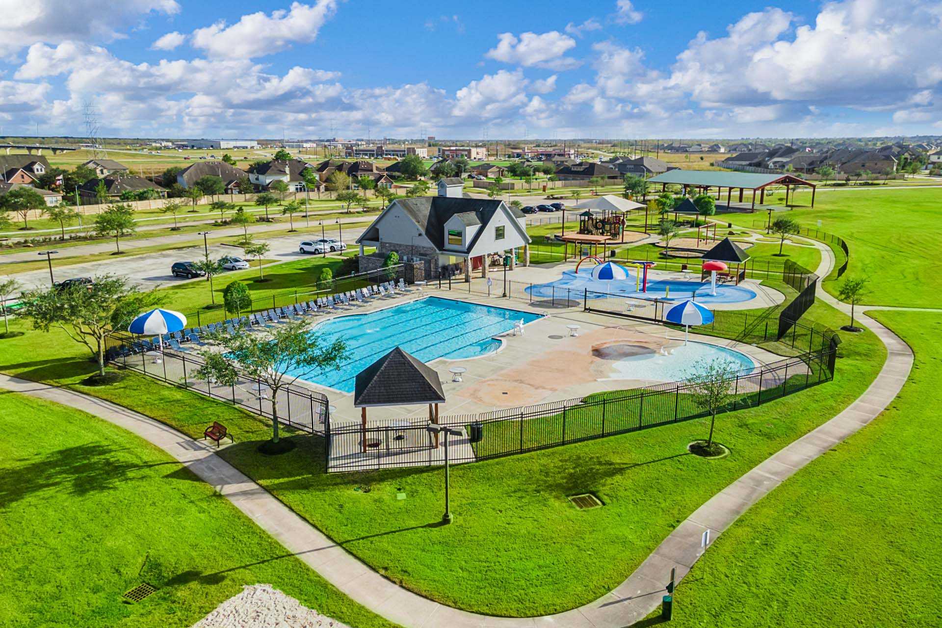 Resort-style pool and clubhouse at Sierra Vista in Rosharon Texas by Davidson Homes with lounge chairs kids splash pad and green lawns