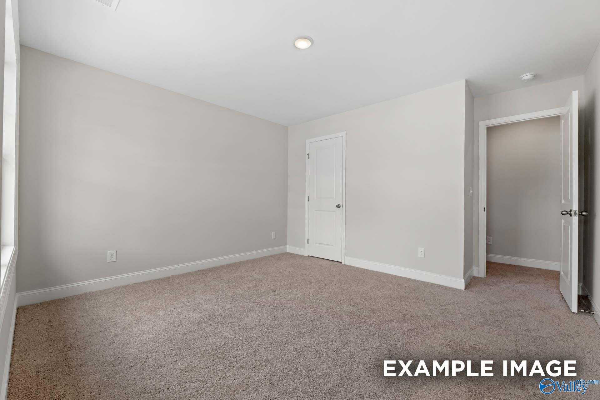 Bright secondary bedroom with light gray walls, beige carpet, and walk-in closet in Davidson Homes The Camden, Huntsville, Alabama