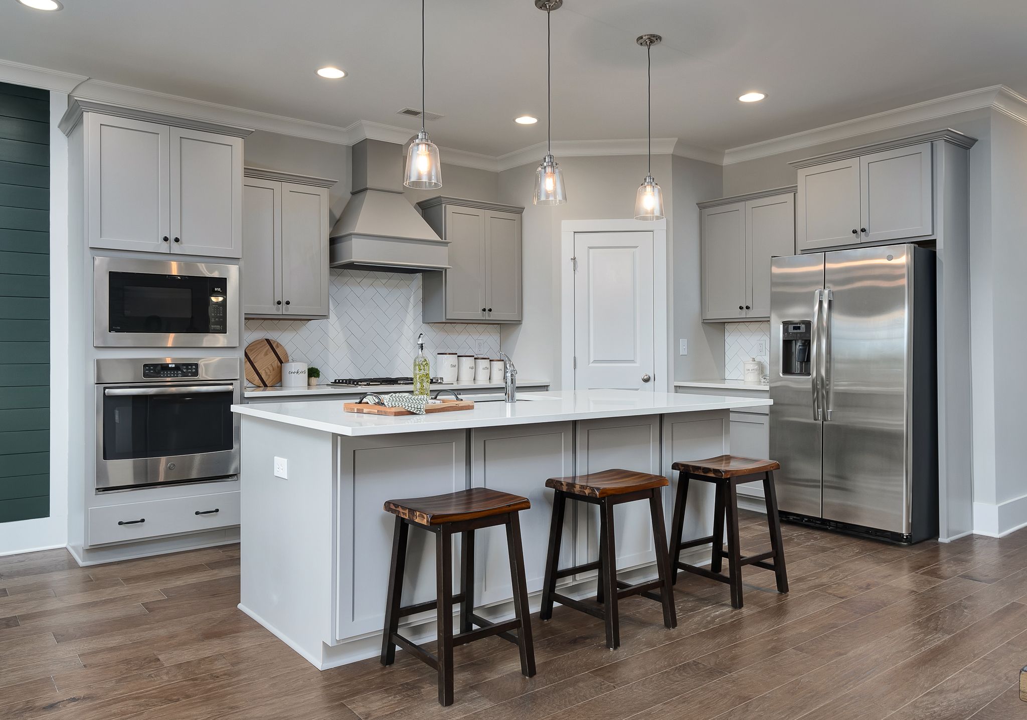 Modern kitchen at Chimney Creek in Hampton Cove AL with white island, stainless appliances, pendant lights and hardwood floors