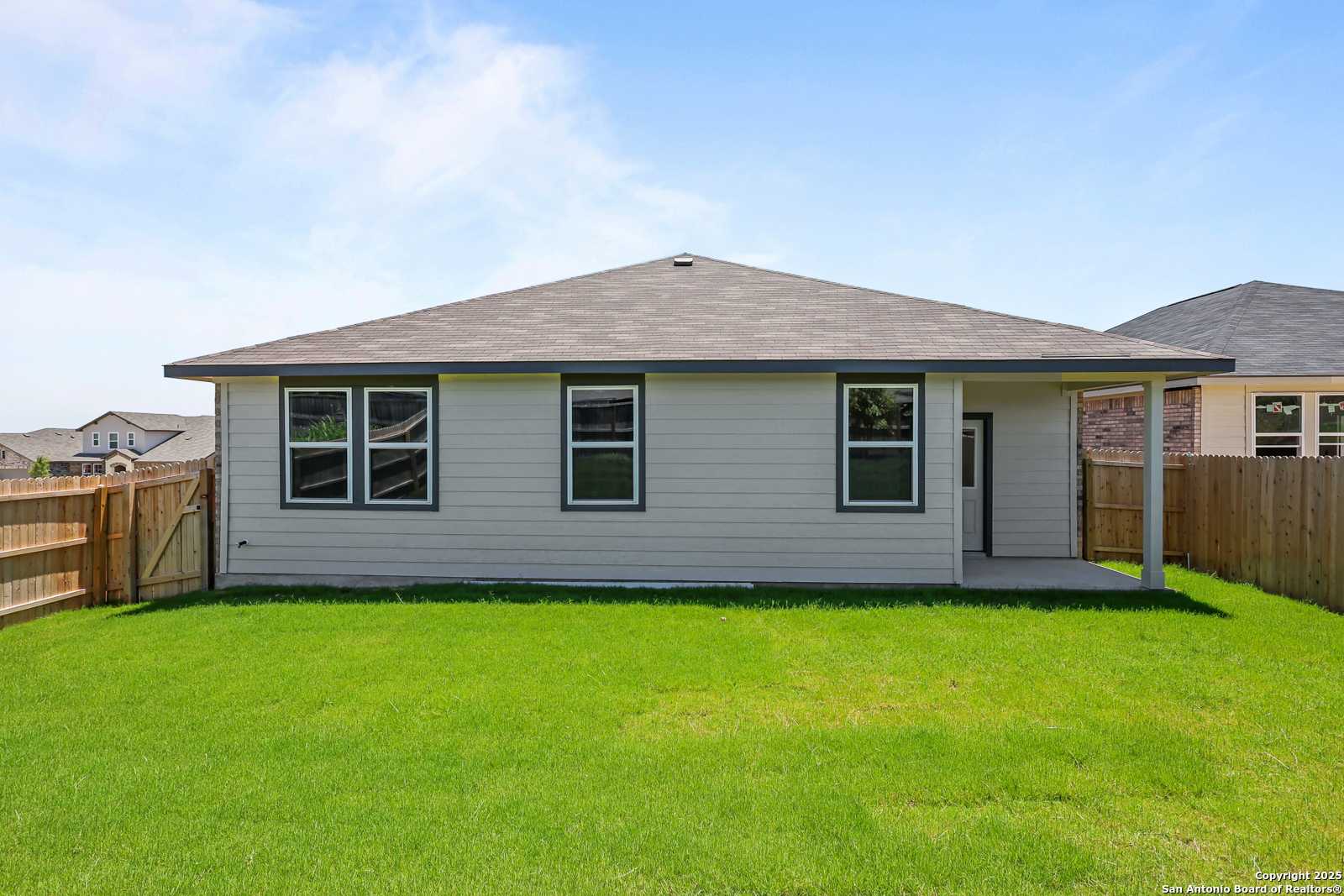 Rear view of The Daphne K single-story home with covered patio, large windows, and lush green backyard in Comanche Ridge, San Antonio, Texas