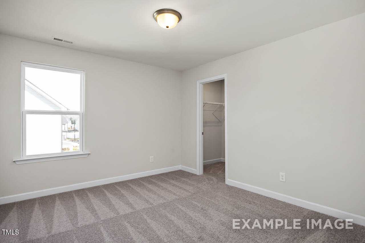 Bright secondary bedroom with neutral walls, carpet floor, large window, and open closet in The Hickory II B, Lillington, NC
