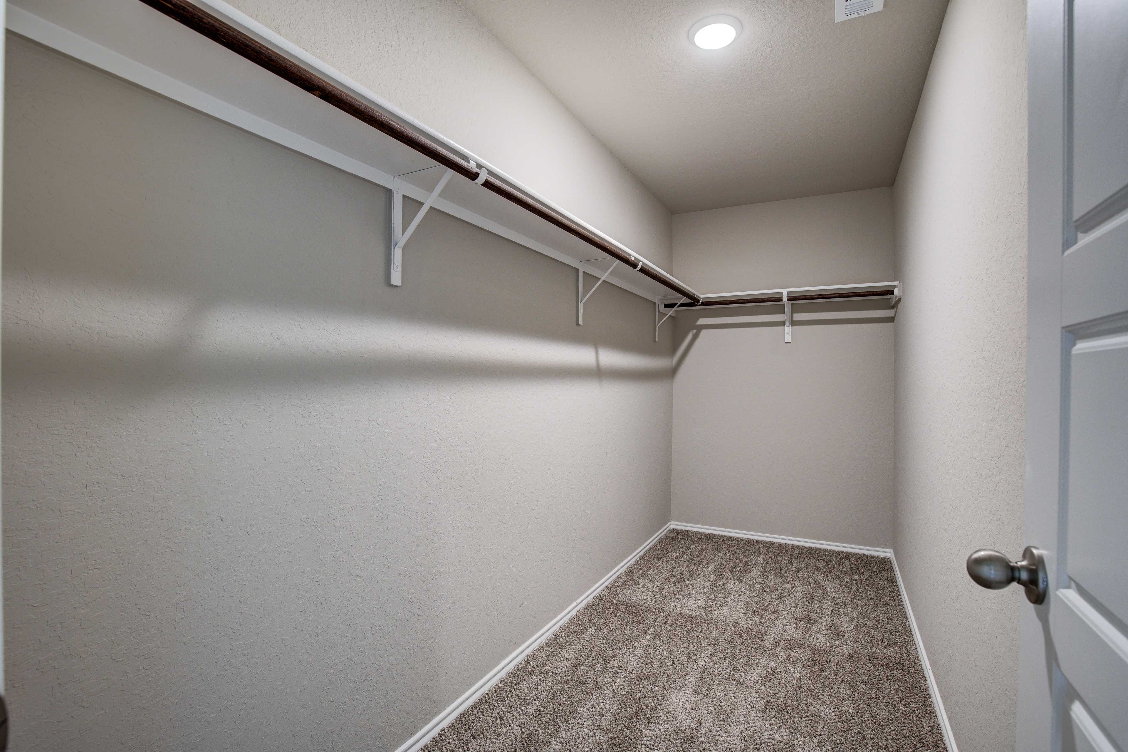 Spacious walk-in closet in The Murray home design featuring beige walls, white shelving rods, and carpeted flooring
