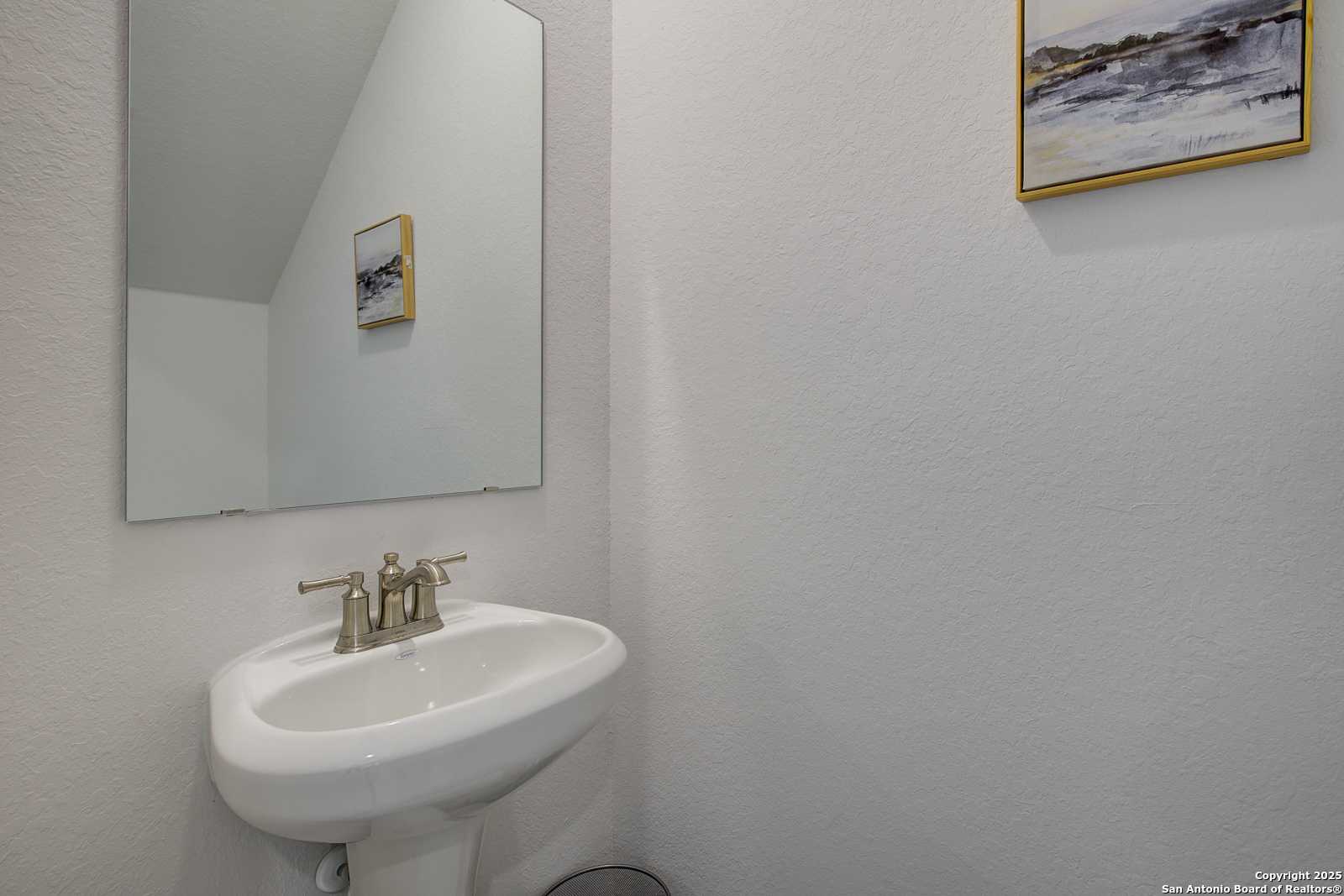 Modern powder room with white pedestal sink, framed mirror, and abstract art in Davidson Homes The Trinity A, San Antonio