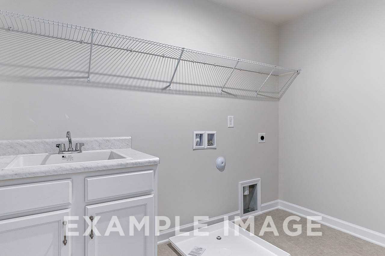 Spacious laundry room in The Willow C home with utility sink, white cabinets, wire shelving, and beige walls
